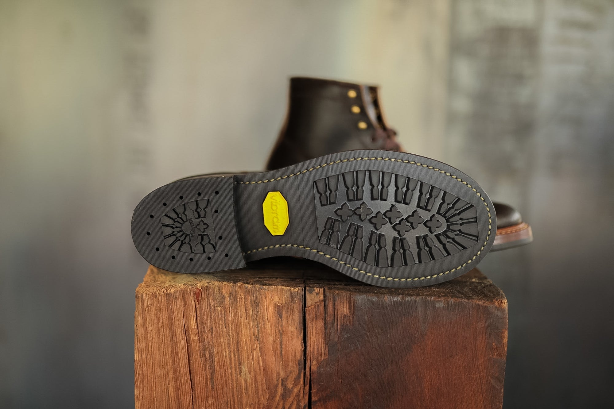Close-up of a boot sole with tread pattern on a wooden block against a blurred background