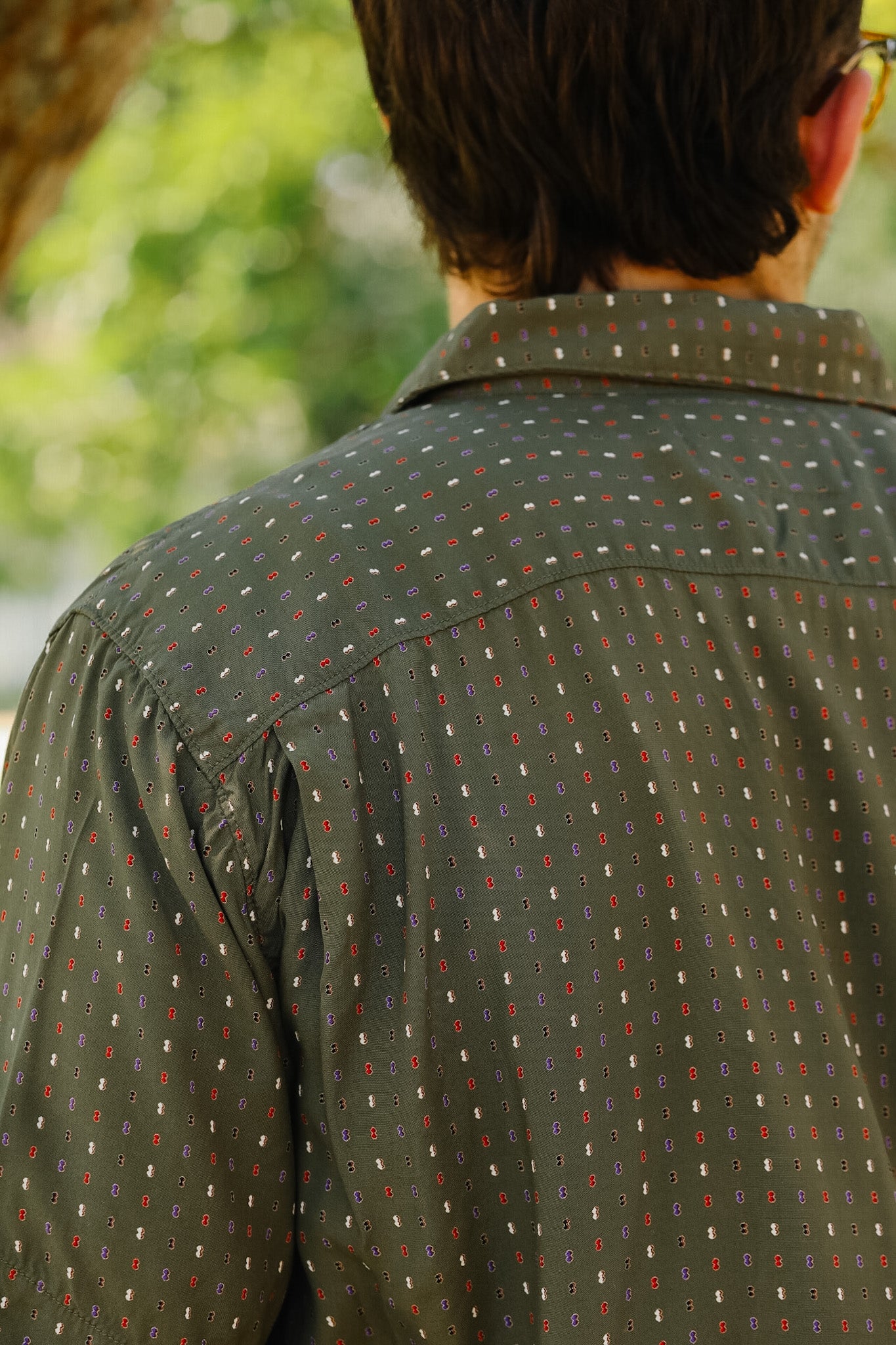 Person wearing a patterned shirt with a blurred natural background