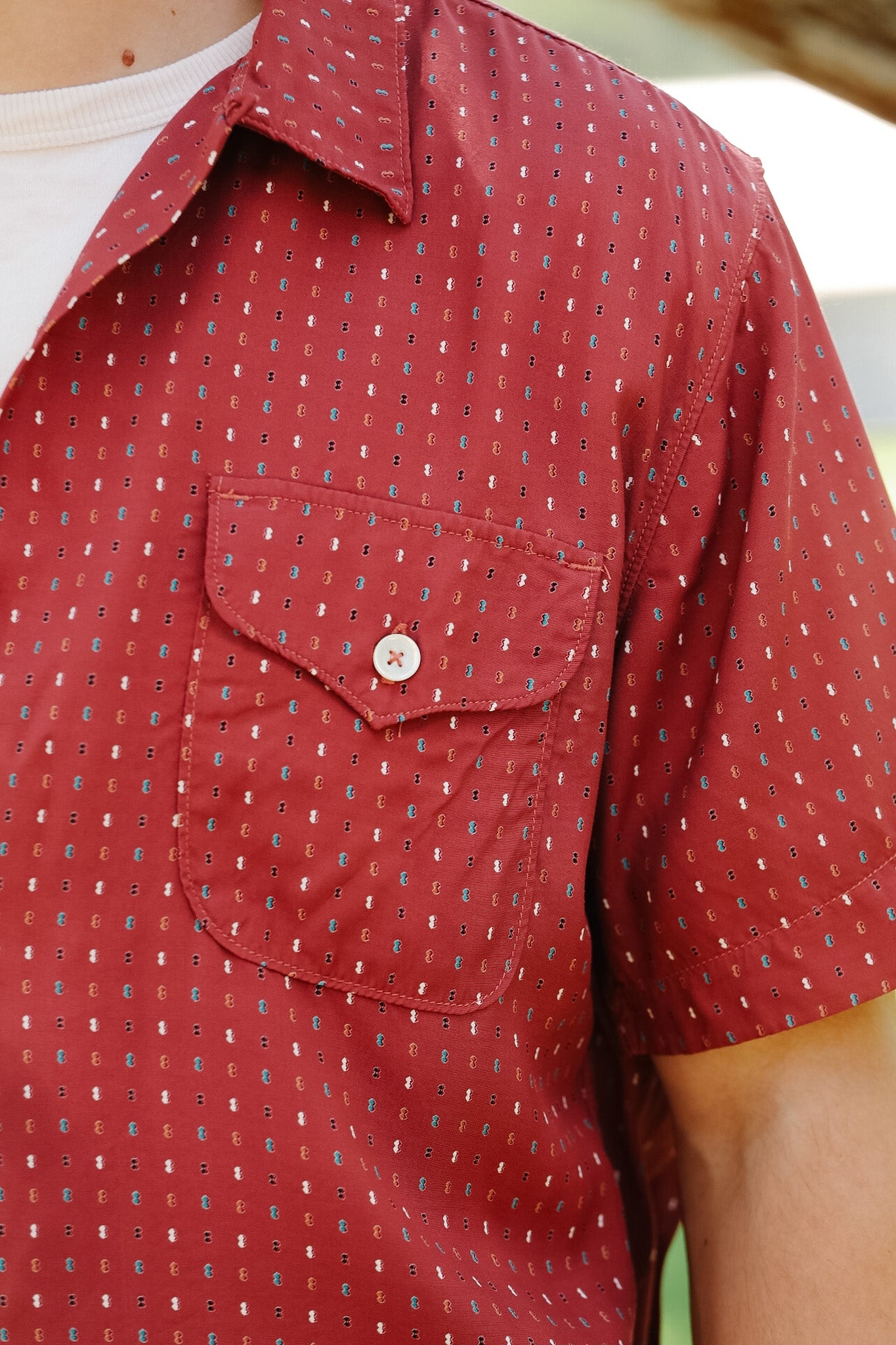 Red patterned shirt with a pocket on a person, blurred background