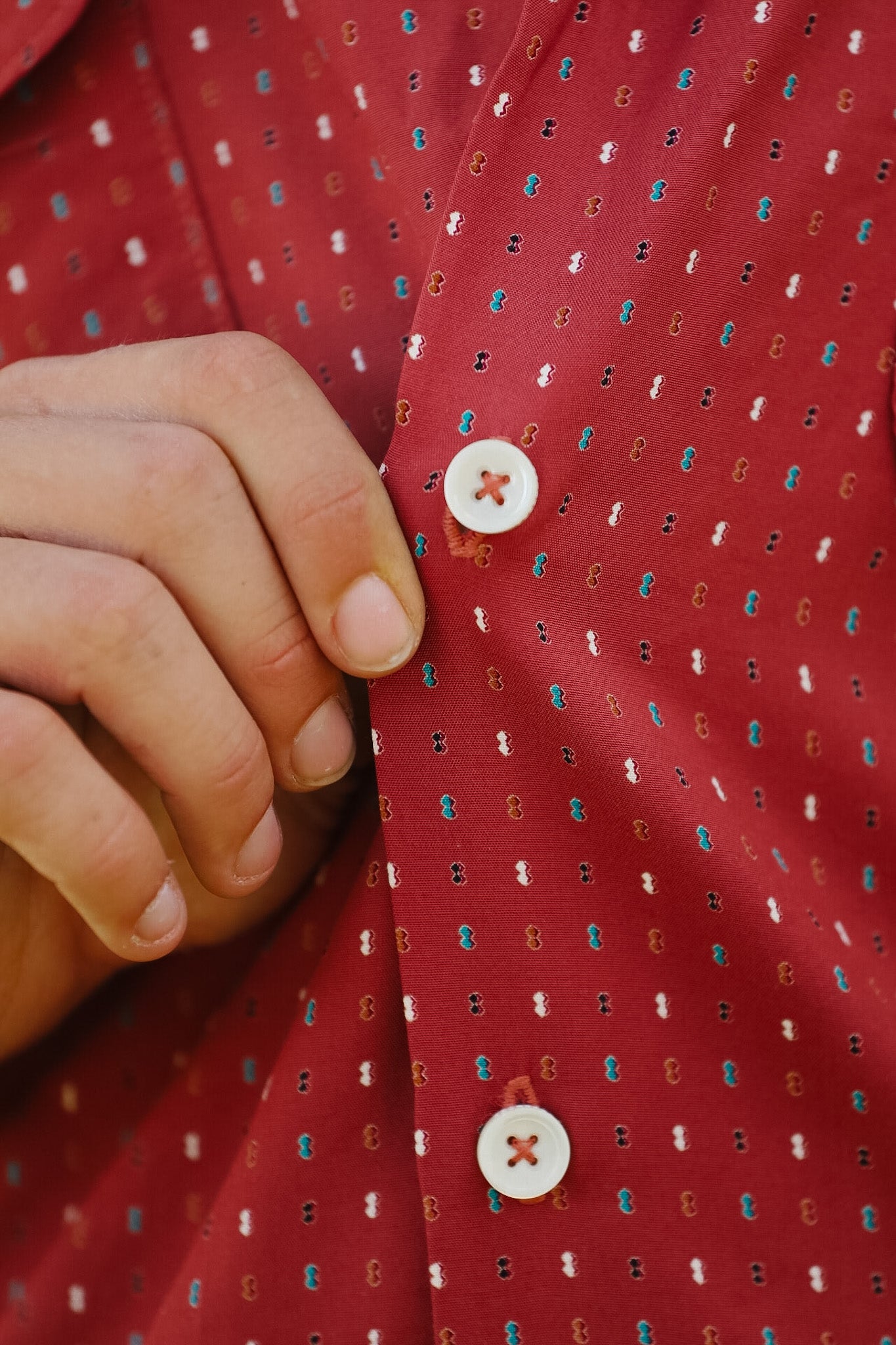 Close-up of a red patterned shirt with a button being adjusted.