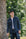 Young man wearing Iron Shop black cap, dark denim shirt, and jeans standing near a tree outdoors