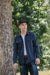 Young man wearing Iron Shop black cap, dark denim shirt, and jeans standing near a tree outdoors