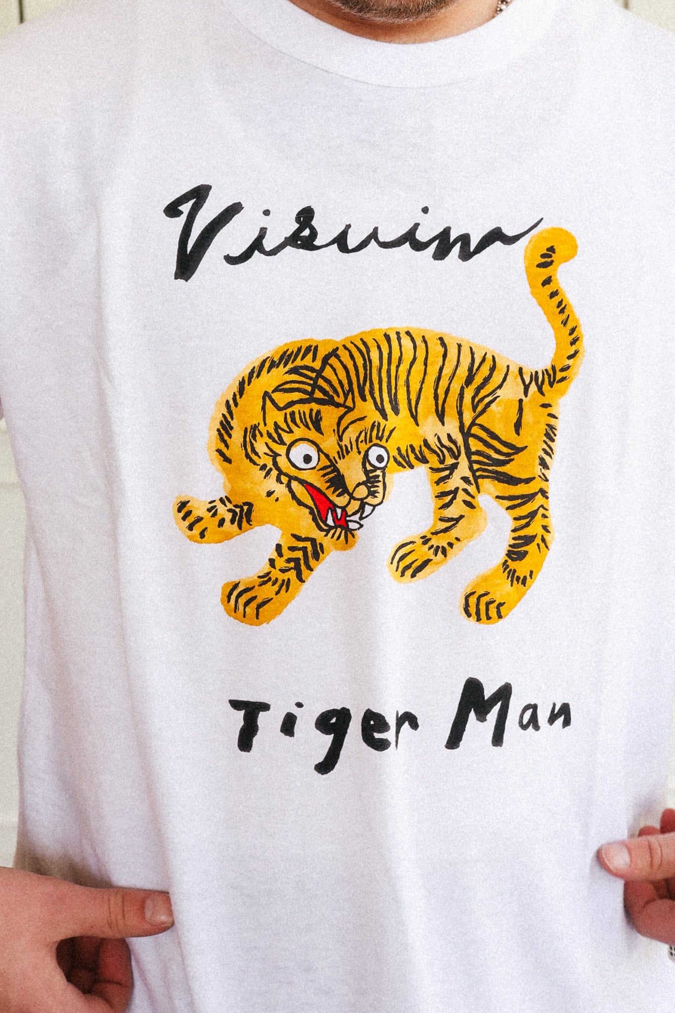 A white crewneck t-shirt featuring a graphic of a yellow and black tiger with the text 'Visuino Tiger Man' printed on the front, worn by a person.