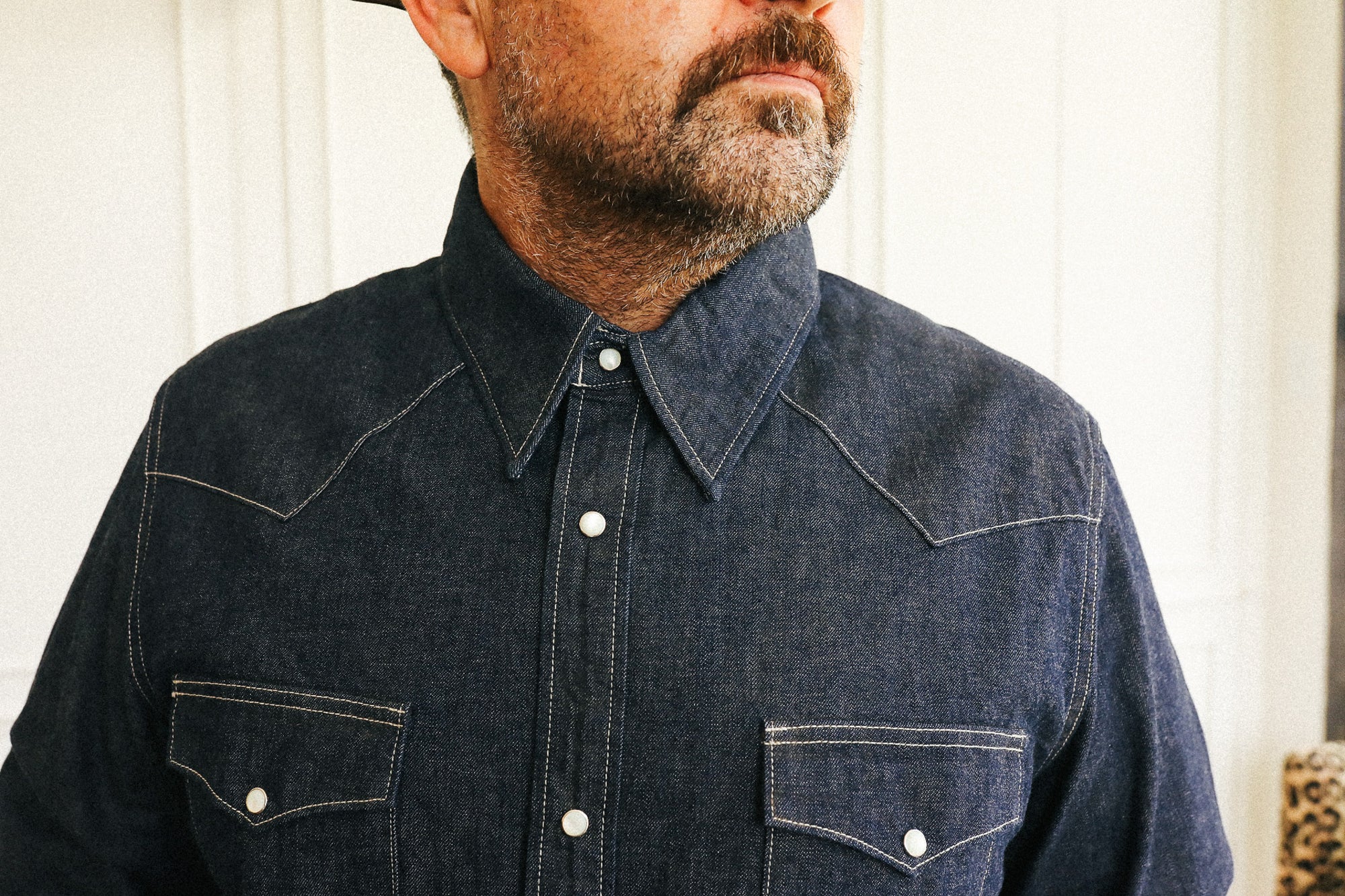 A close-up of a man wearing a dark indigo denim western-style button-down shirt with contrast stitching and two chest pockets.