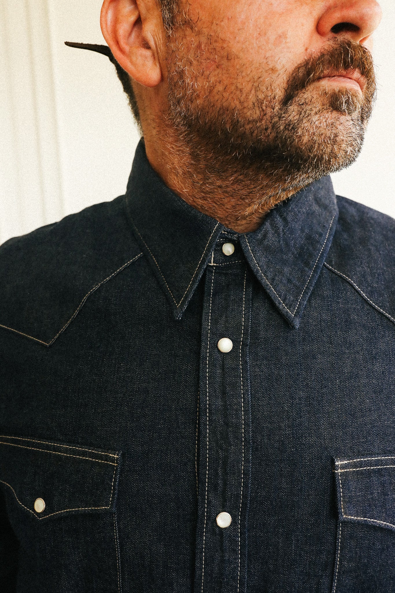 Close-up of a man wearing a dark indigo denim western-style button-down shirt with contrast stitching and white buttons.