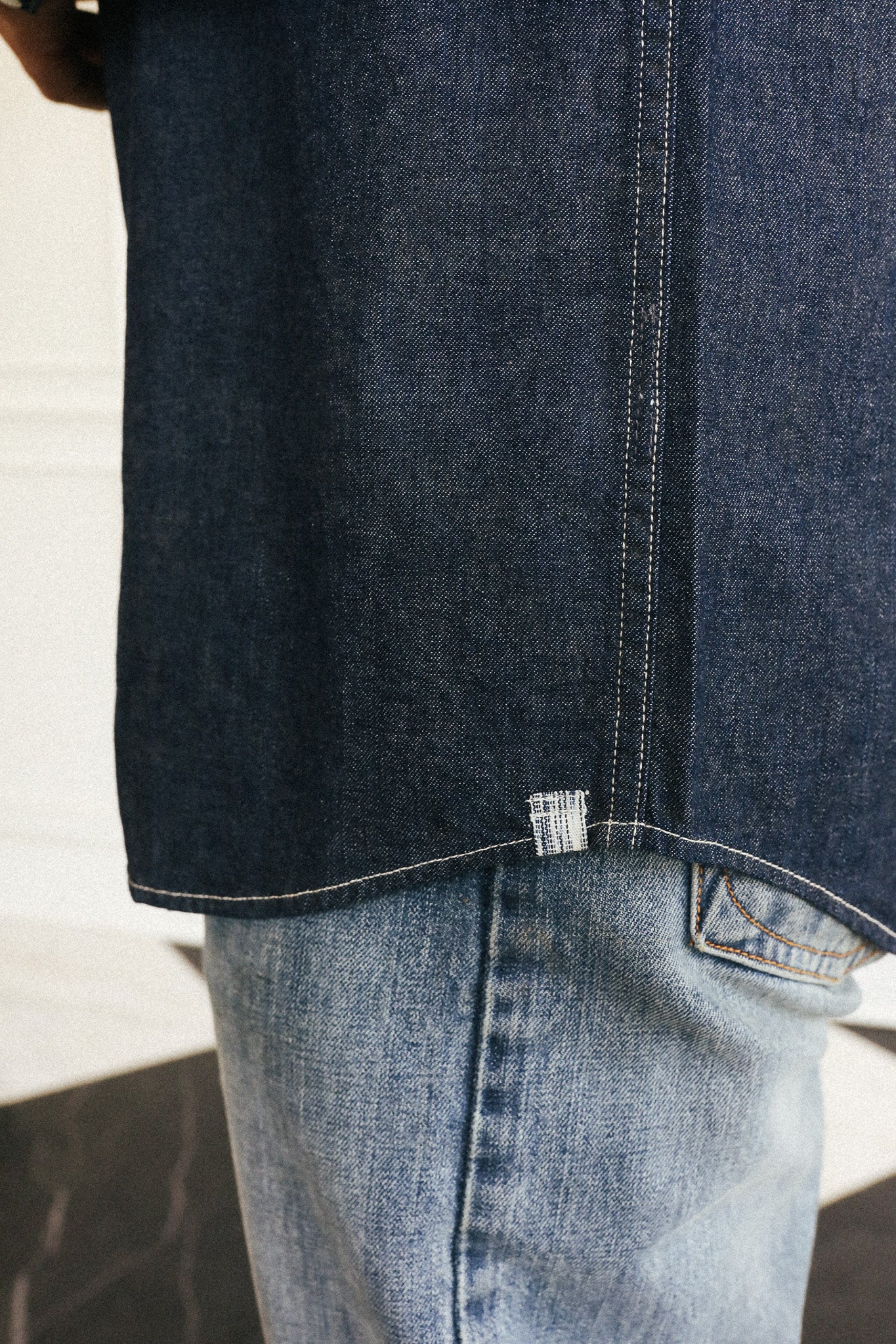 Close-up of a person wearing a dark indigo denim shirt tucked into light-wash blue jeans, showing the hem and contrast stitching.