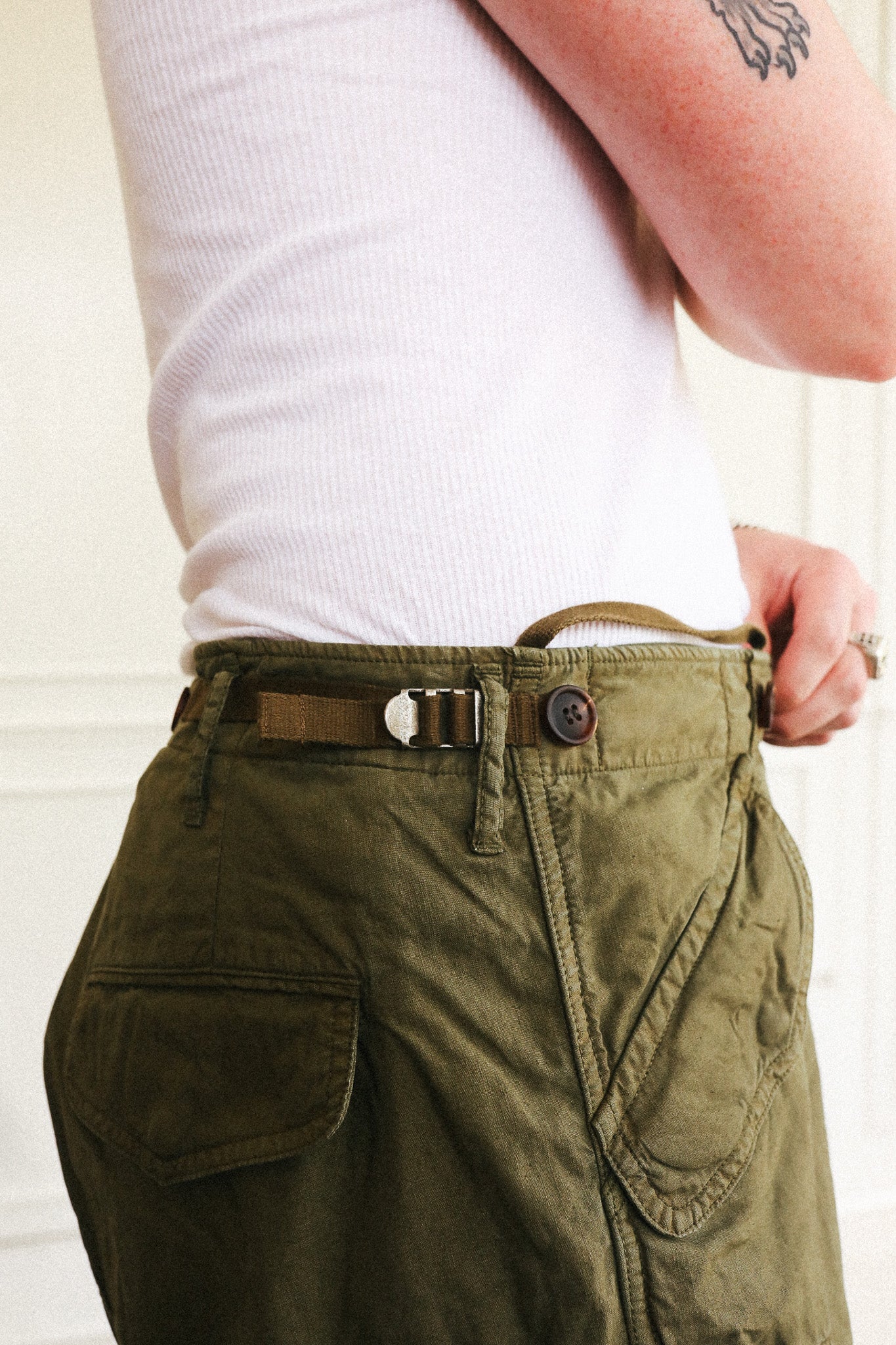 Close-up of a person wearing olive green cargo pants with a brown belt and white ribbed top, shown from the back waist area.