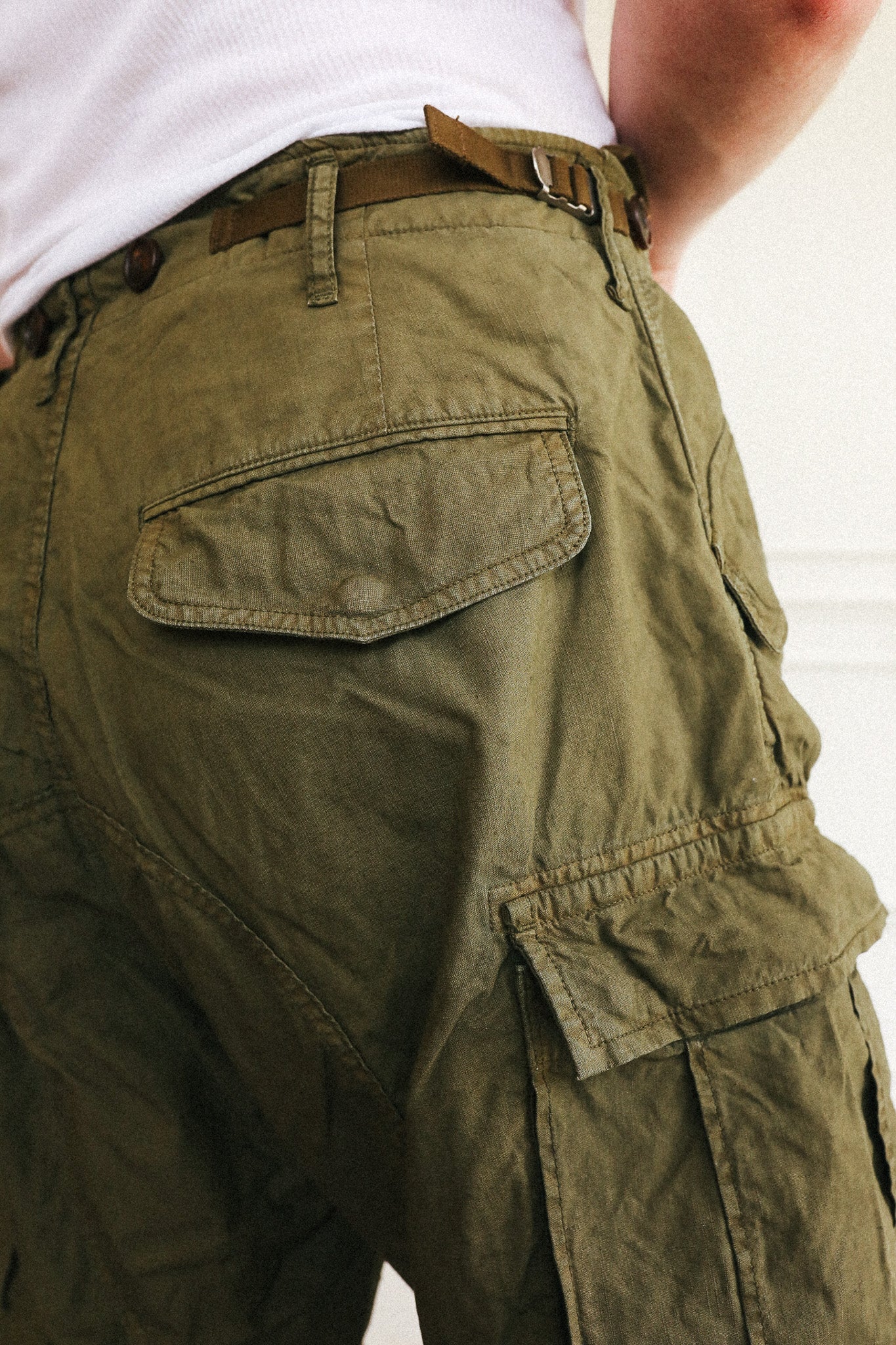Close-up of a person wearing olive green cargo pants with a brown belt, showing the back pocket and side cargo pocket details.