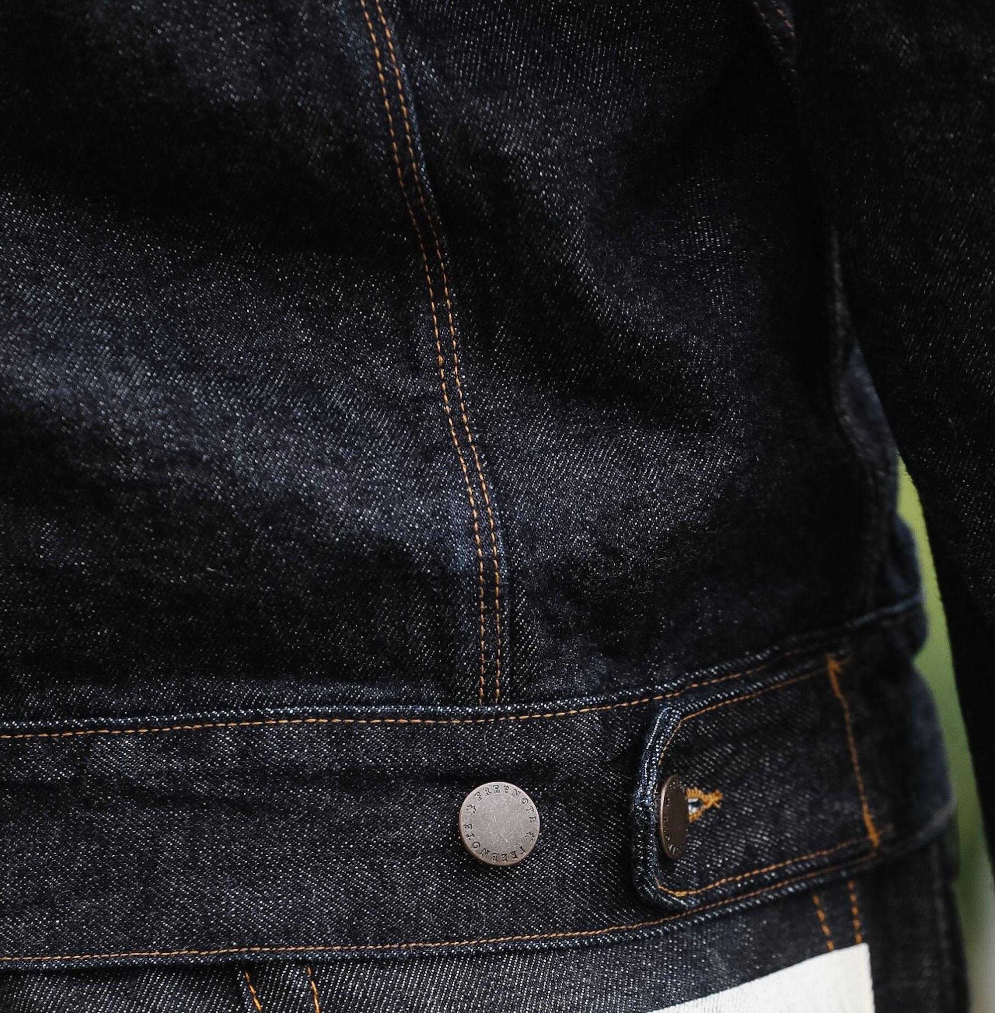 Close-up of a dark denim jacket with a button and brand logo.