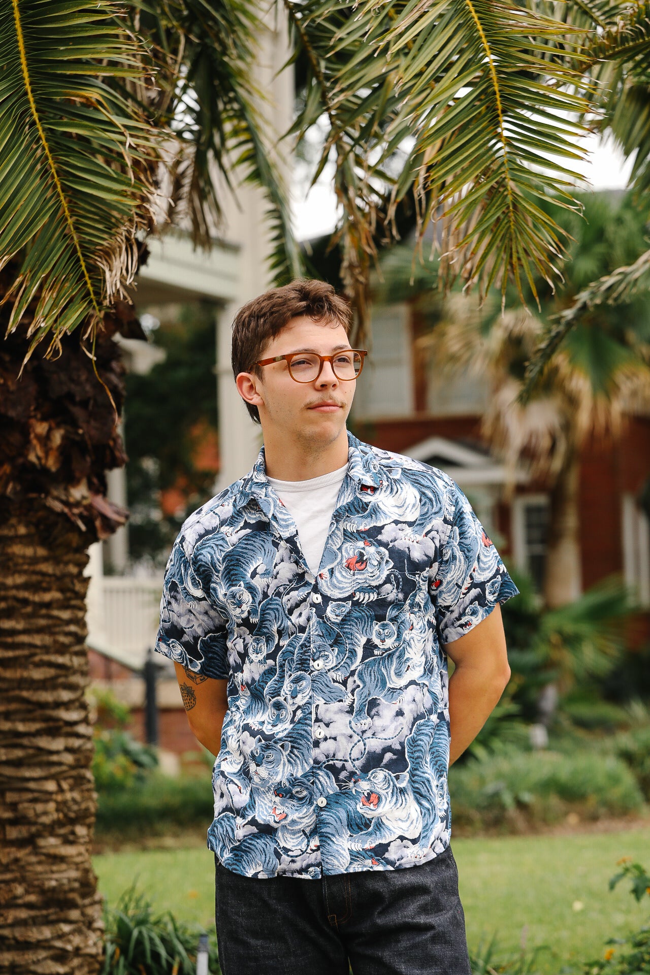 Person wearing a blue floral shirt standing outdoors with palm trees in the background
