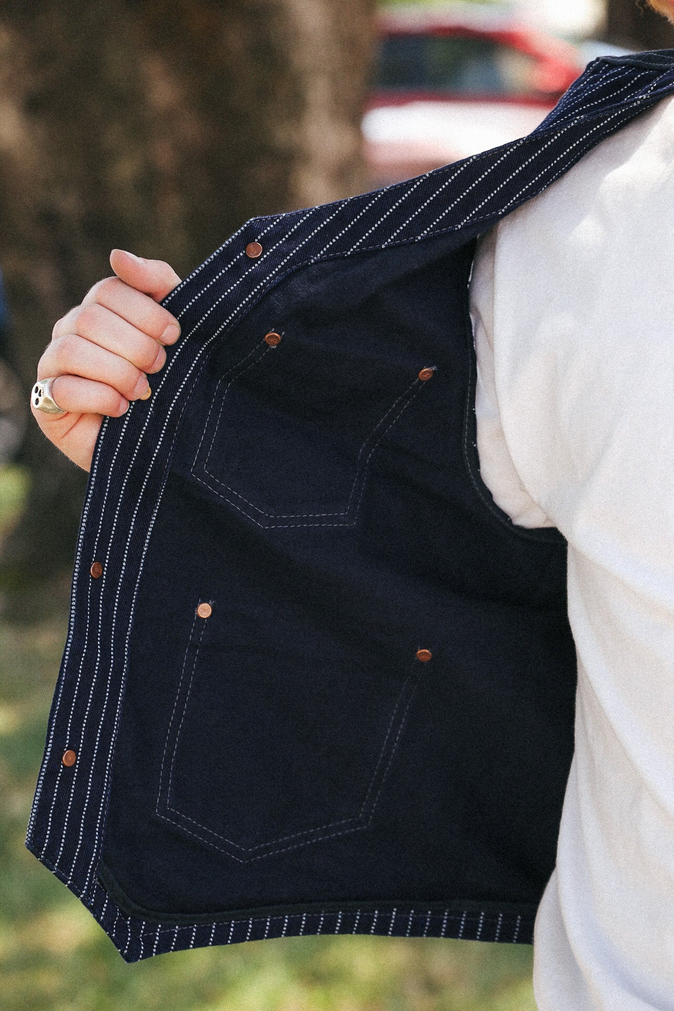 A close-up of a person wearing a dark navy pinstriped vest over a white shirt, holding the vest open to show the interior pockets and stitching.