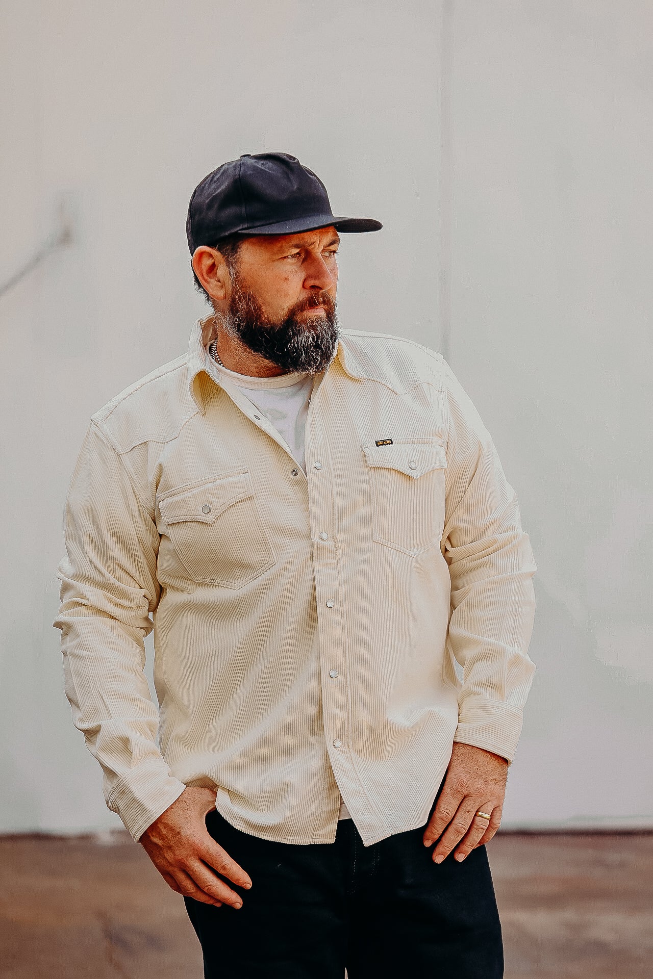 A person wearing an off white corduroy western shirt with pearl snap fastenings, standing against a plain background.