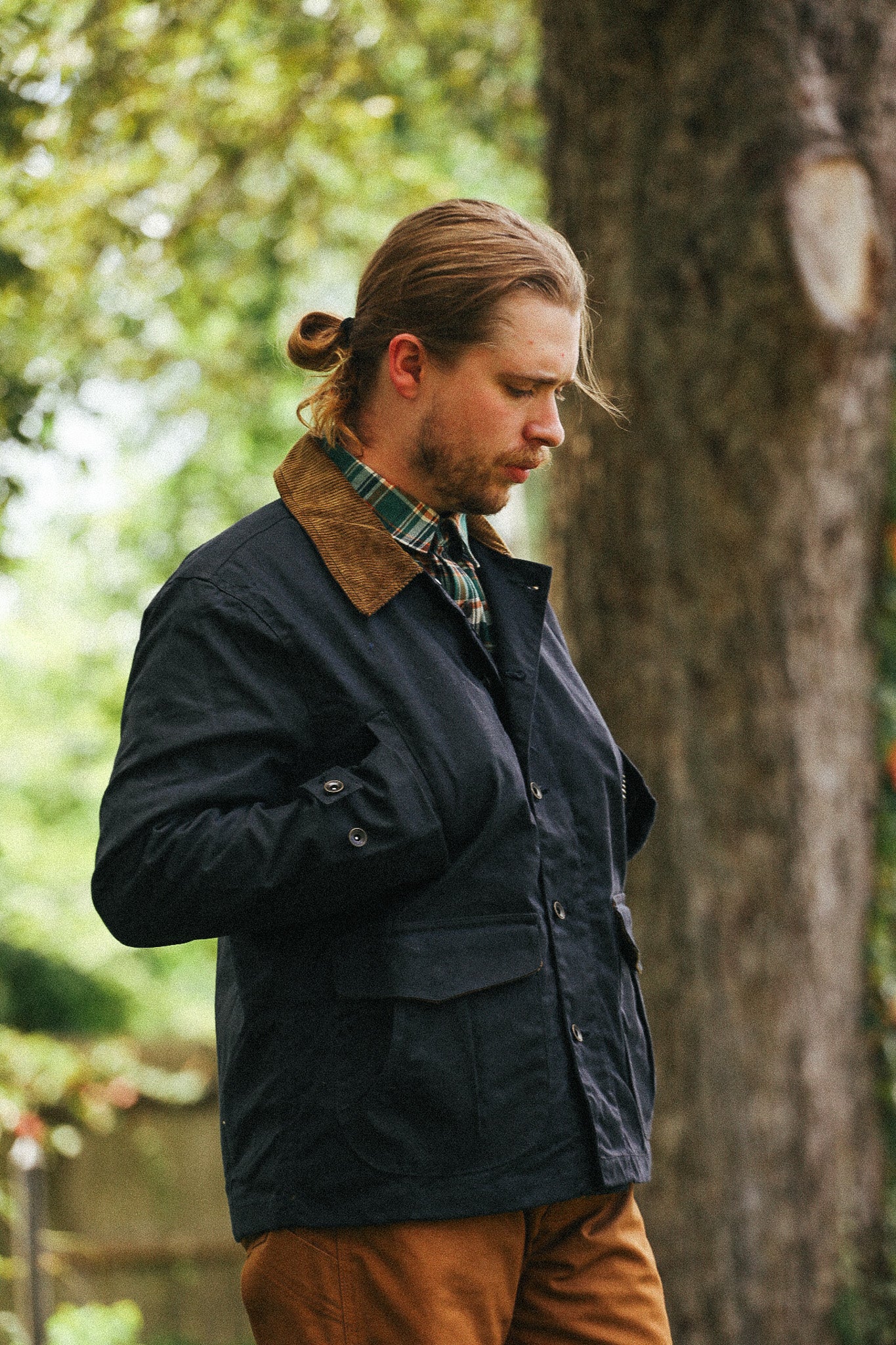 man standing with black jacket and green shirt against a green natural background