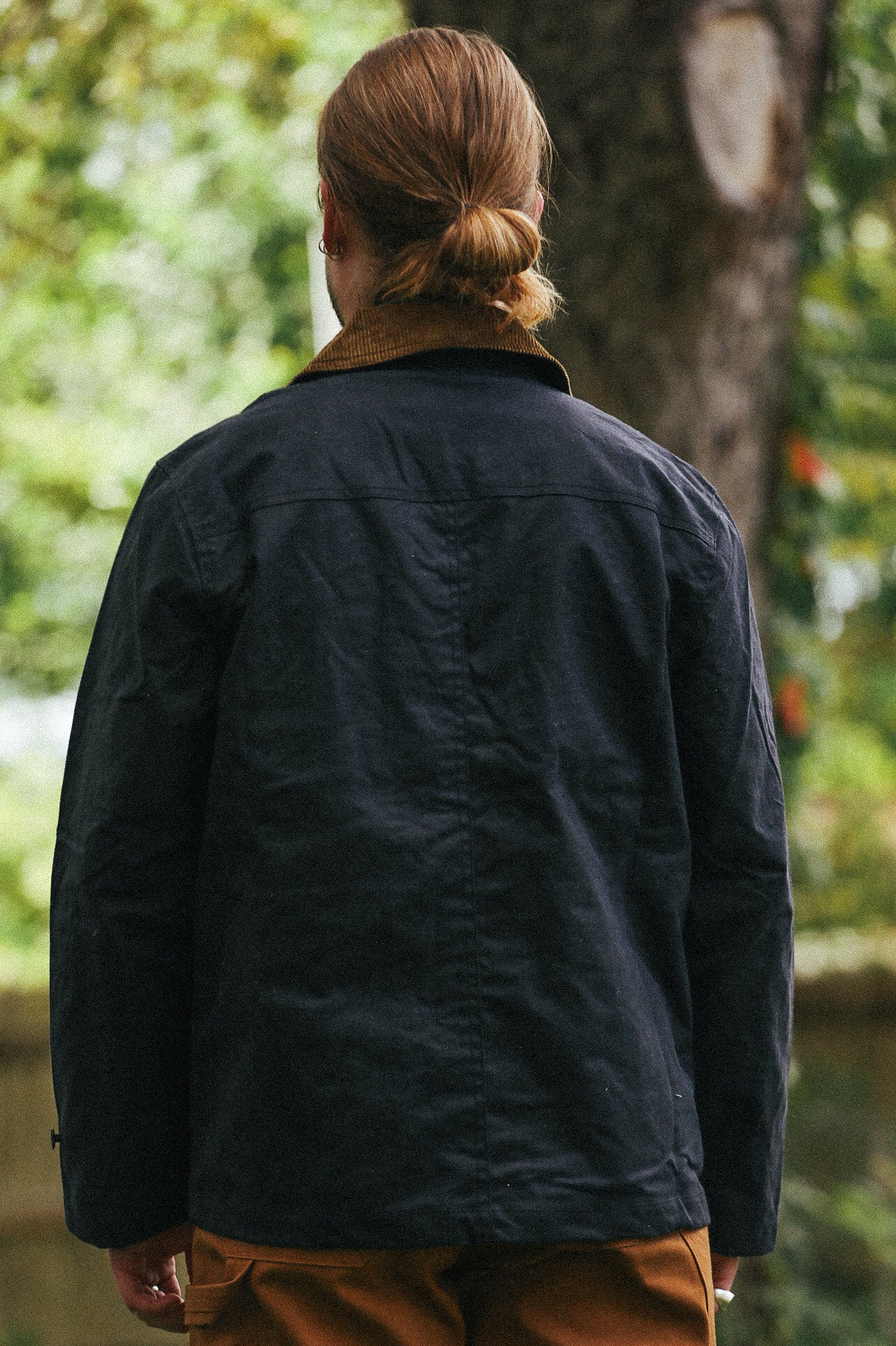 man standing with black jacket and green shirt against a green natural background