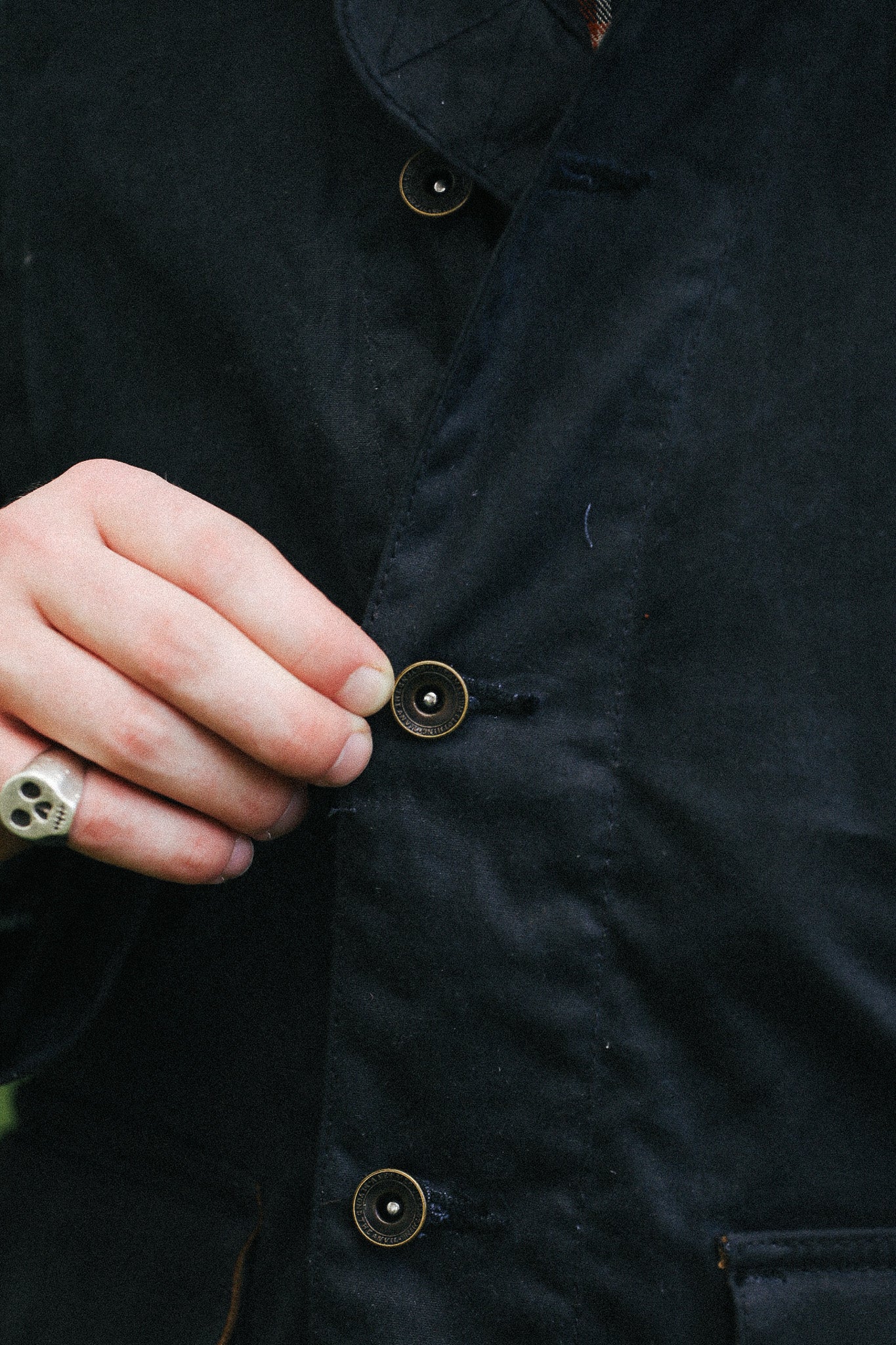 man with black jacket with showing button detail against a green natural background