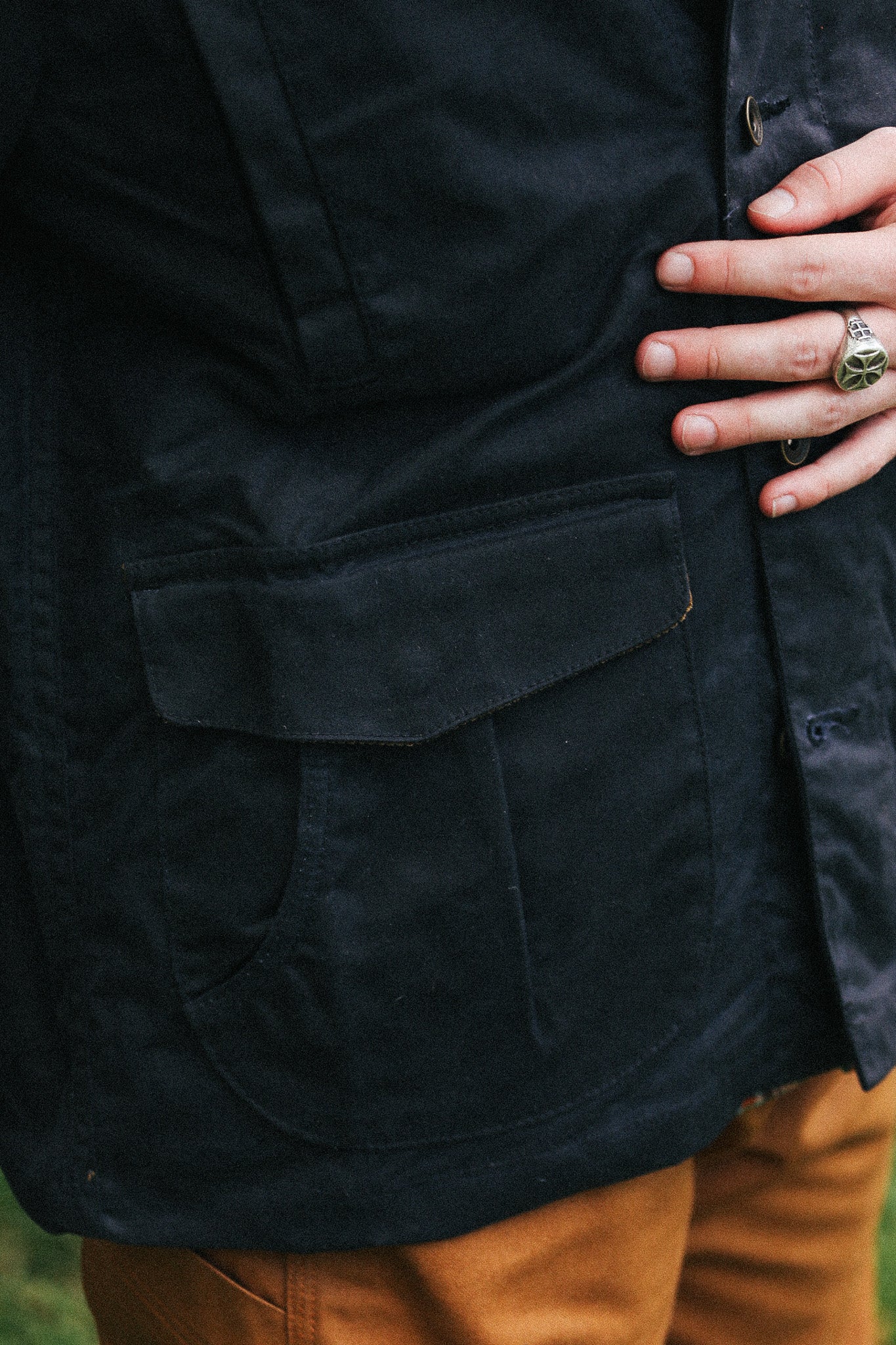 man with black jacket with showing pocket detail against a green natural background