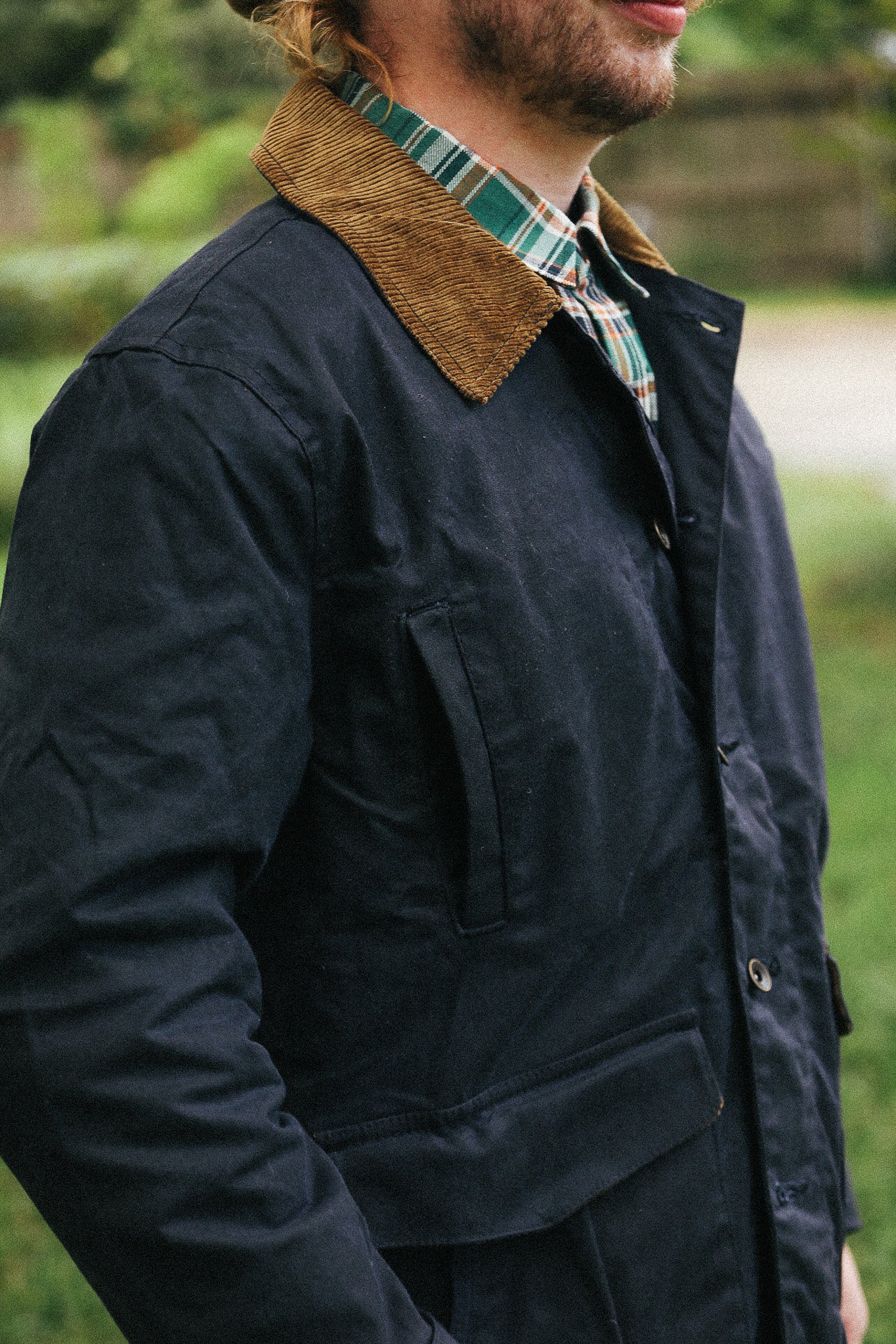 man with black jacket with showing pocket detail against a green natural background