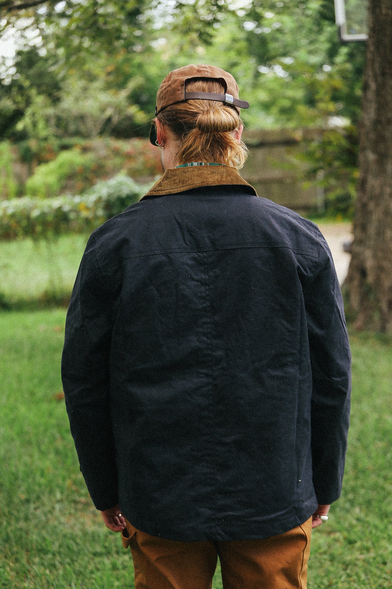man with black jacket with showing back detail against a green natural background