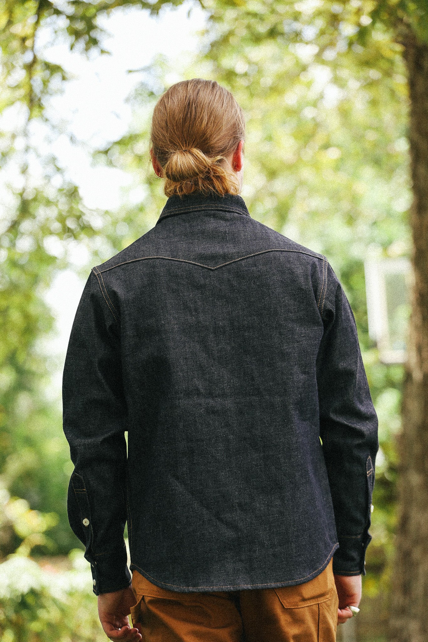 man with denim shirt facing away  against a green natural background