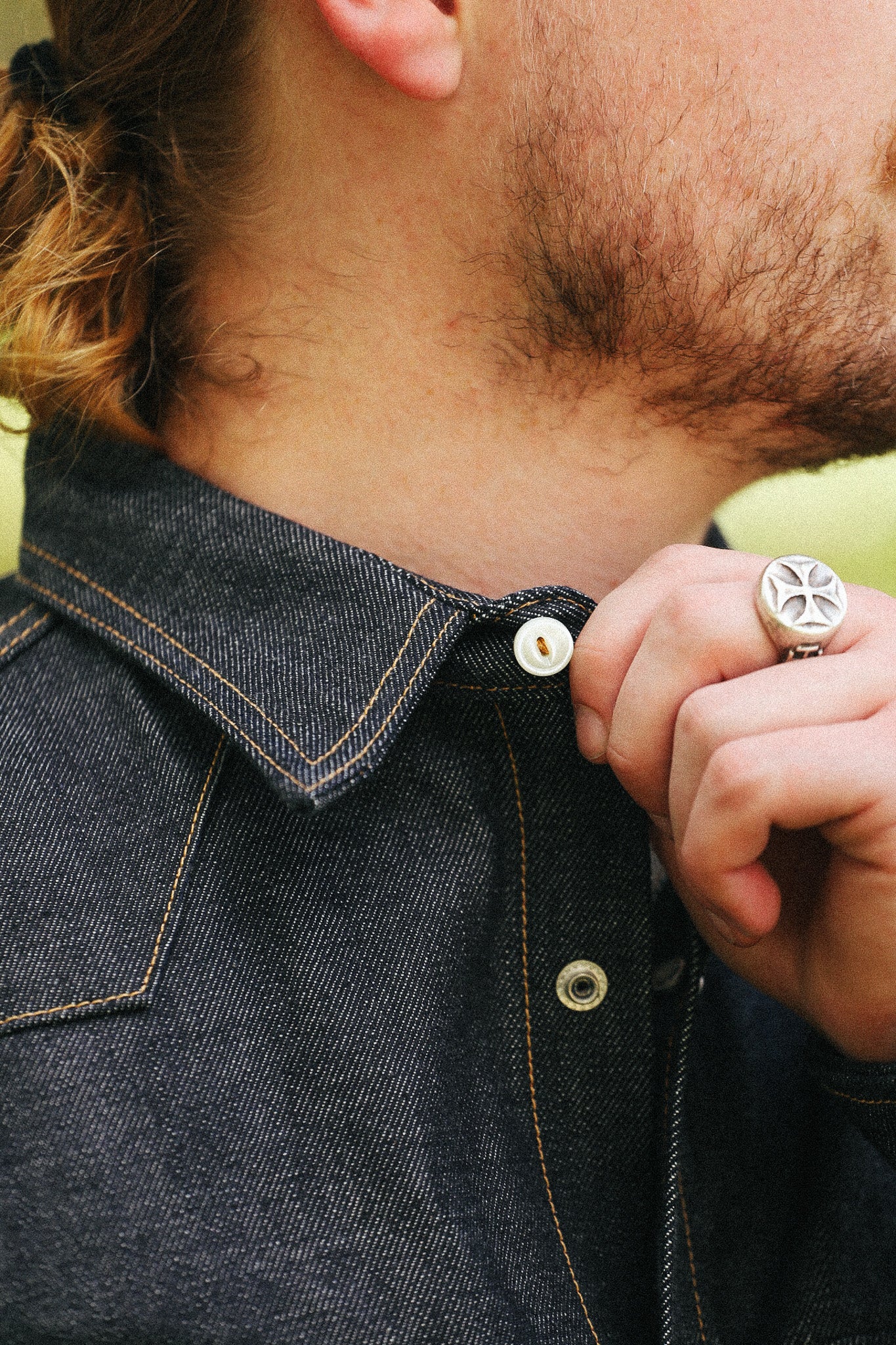 man with denim shirt showing collar detail against a green natural background