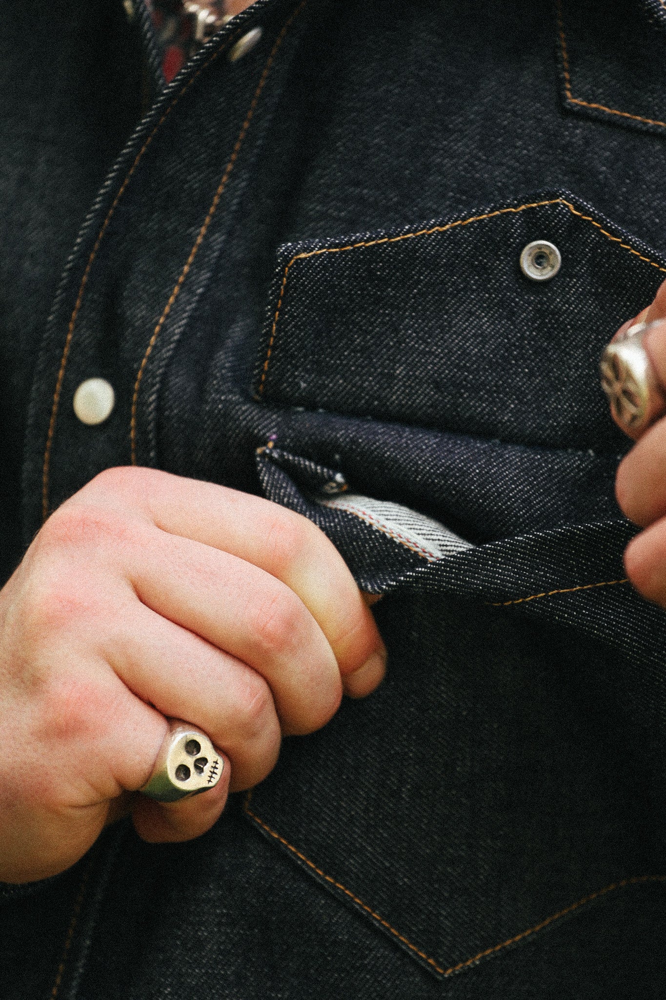 man with denim shirt showing pocket detail against a green natural background