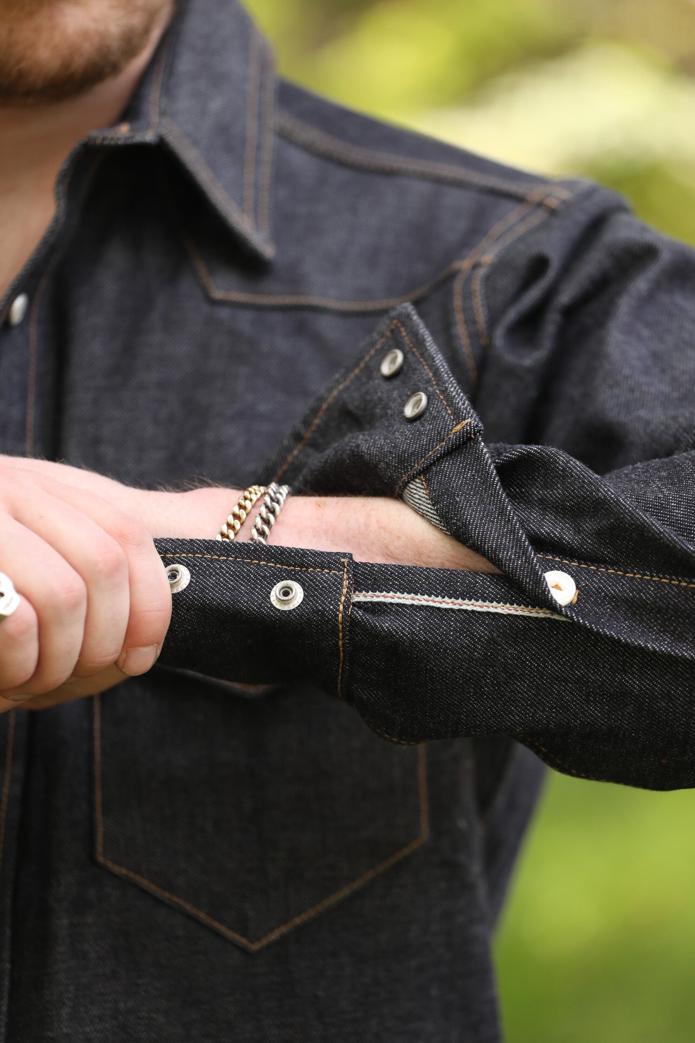 man with denim shirt showing cuff detail against a green natural background