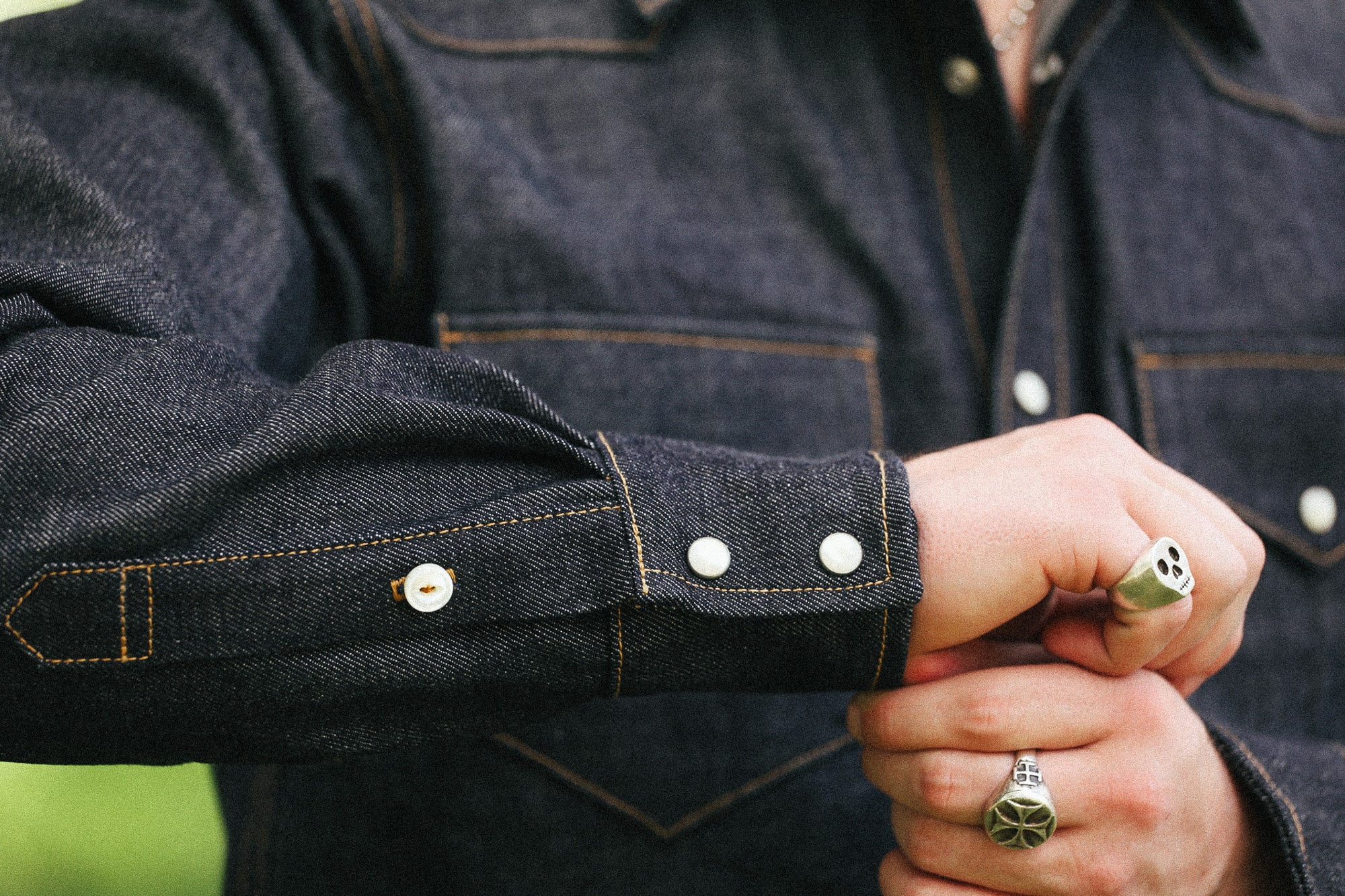 man with denim shirt showing cuff detail against a green natural background