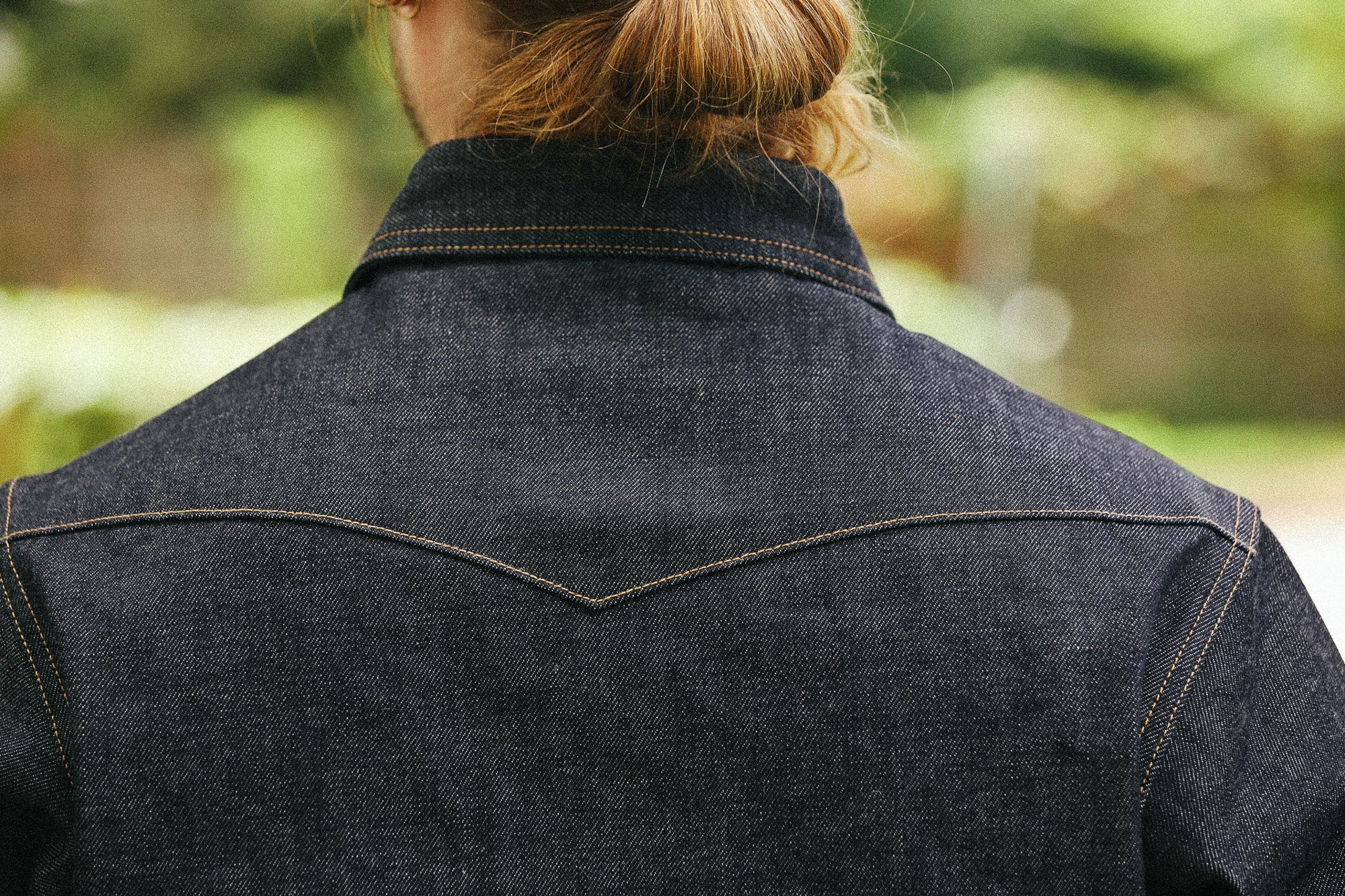 man with denim shirt showing back detail against a green natural background