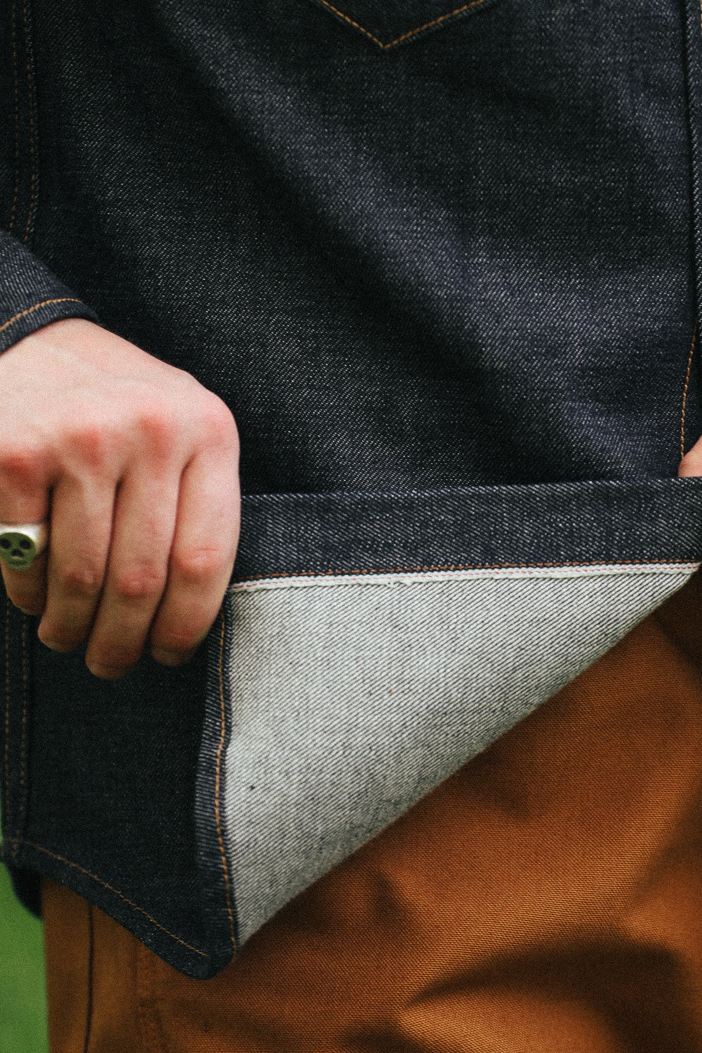 man with denim shirt showing cuff detail against a green natural background