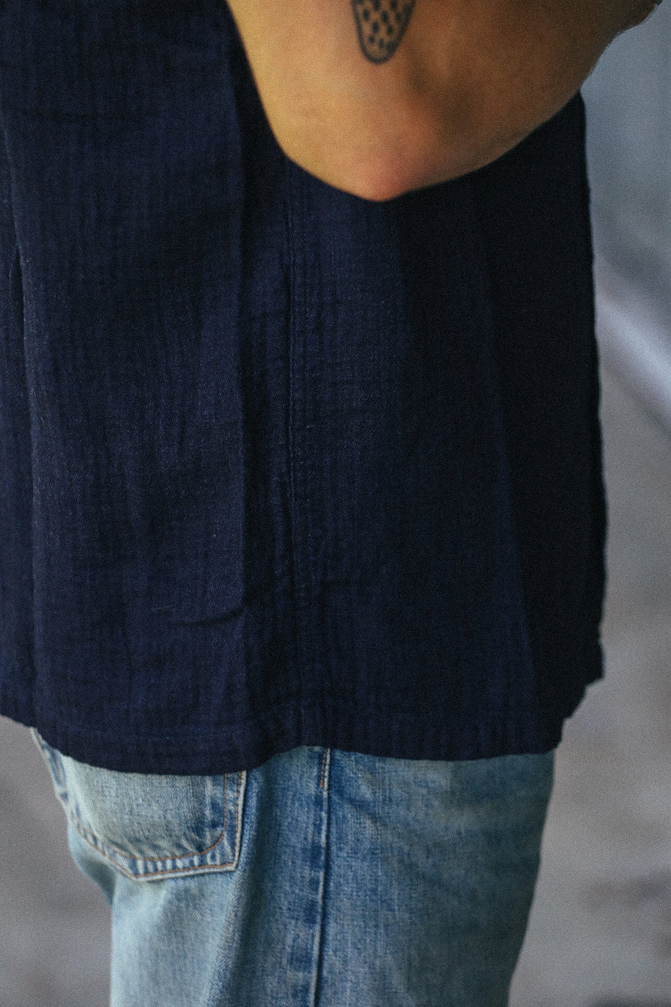 Close-up of a person wearing a dark navy blue sleeveless top with light blue denim jeans, showing the fabric texture and side pocket detail.