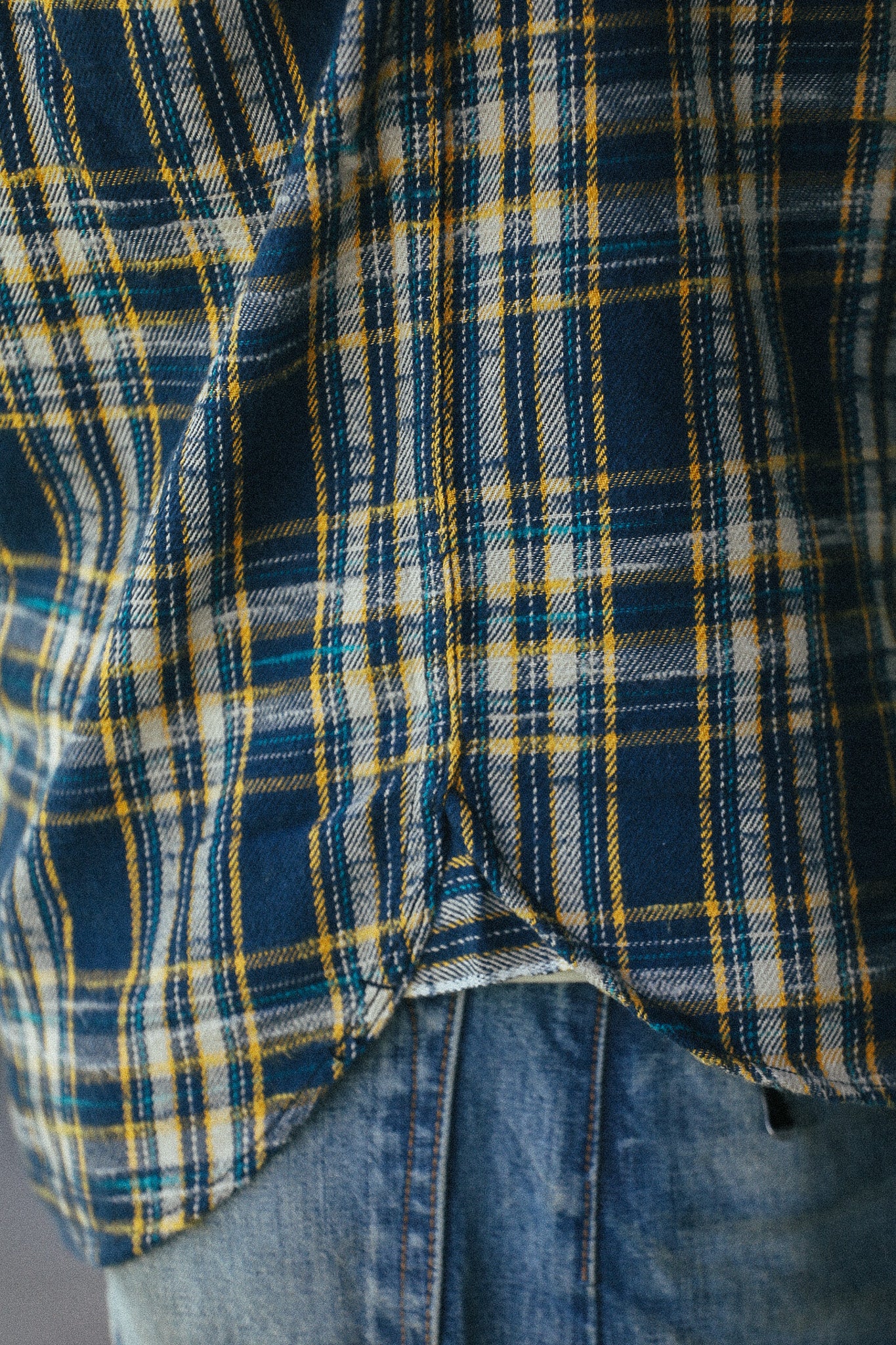 Close-up of a blue, yellow, and white plaid flannel shirt worn over blue jeans.
