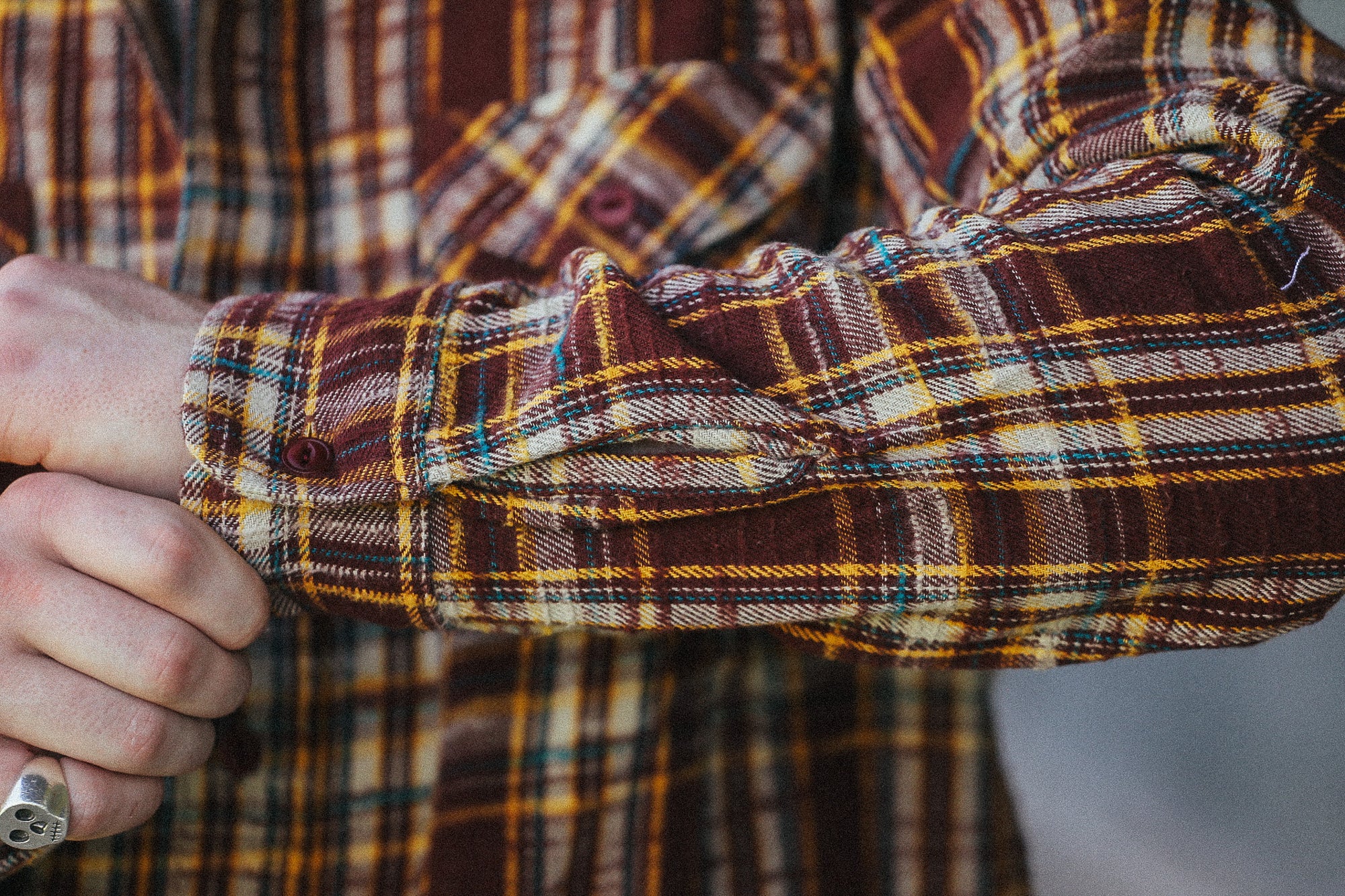 Close-up of a person's arm and hand adjusting the cuff of a brown, yellow, and black plaid flannel shirt.