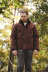 A man wearing a brown corduroy jacket with a dark brown fur collar, standing outdoors in a wooded area.