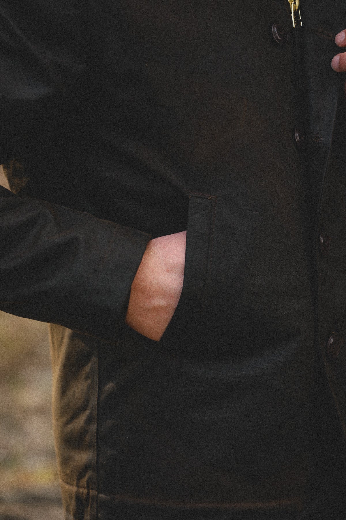 Close-up of a person wearing a dark brown waxed canvas jacket, with one hand tucked into a side pocket.