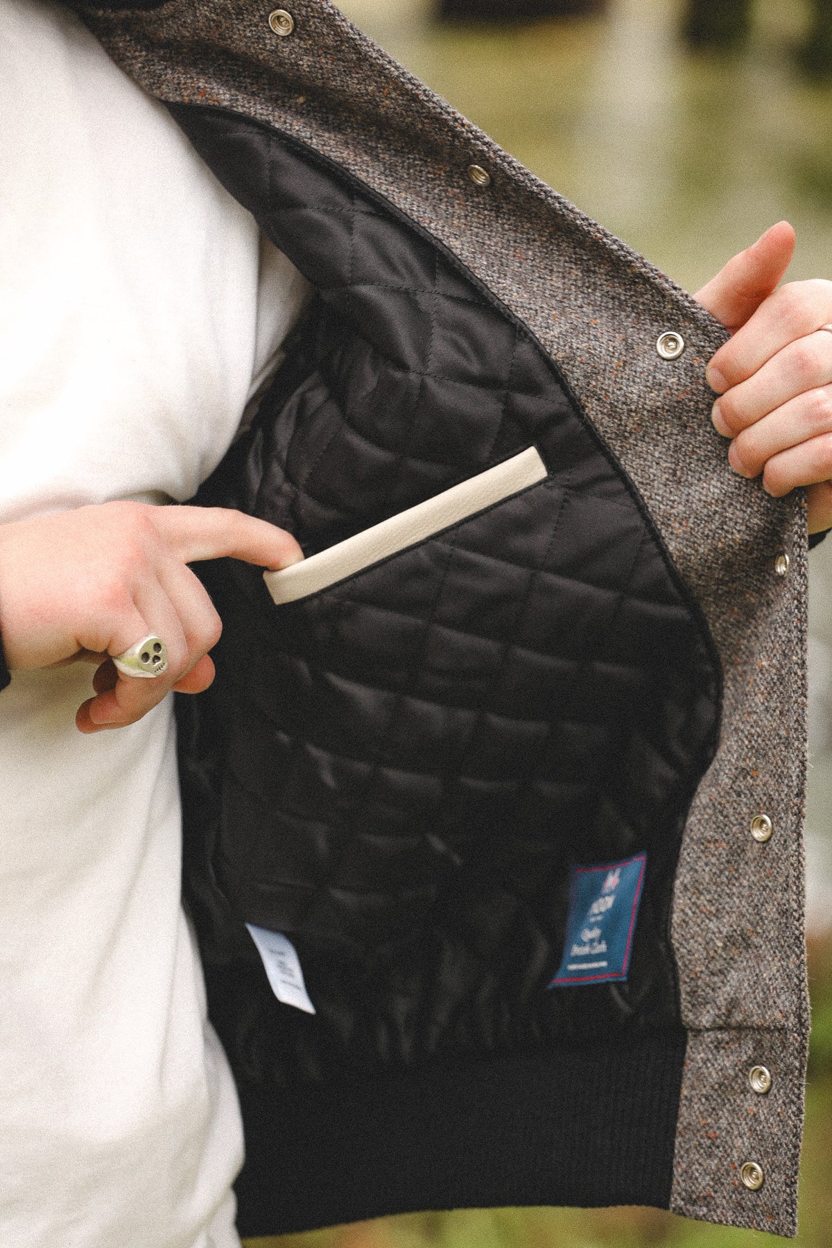 Close-up of a person opening a tweed jacket to show the black quilted interior lining and a light beige pocket flap.