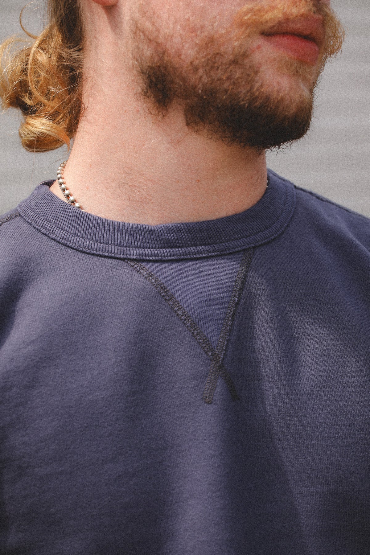 Close-up of a person wearing a dark slate blue crewneck sweatshirt, showing the ribbed collar and textured fabric.