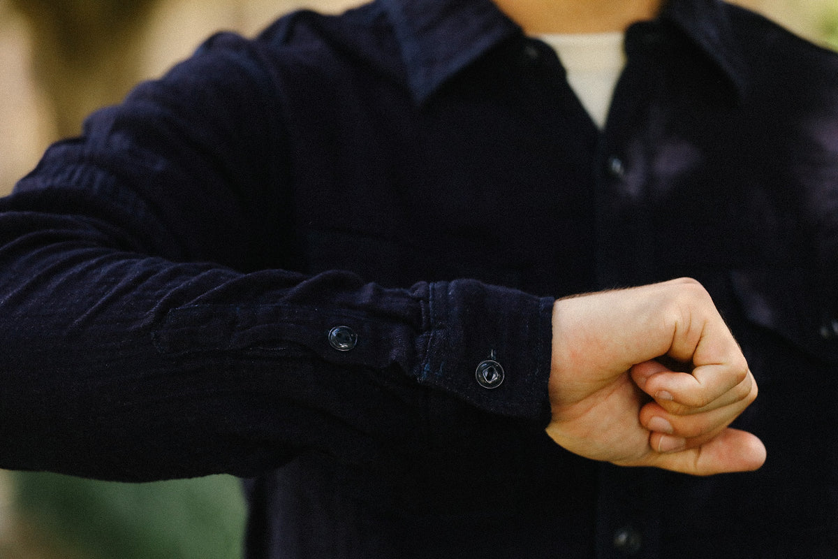 A close-up of a person wearing a dark navy corduroy button-up shirt over a white undershirt, with their hand near the cuff of the shirt.
