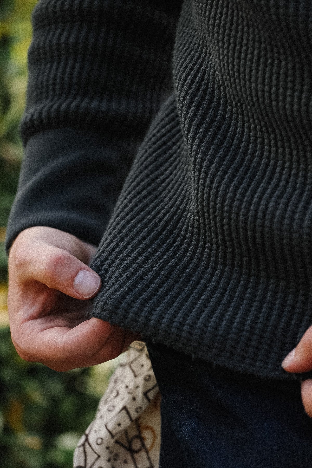 Close-up of a person wearing a dark charcoal gray ribbed knit sweater, showing the texture of the fabric and the cuff being pulled slightly by a hand.