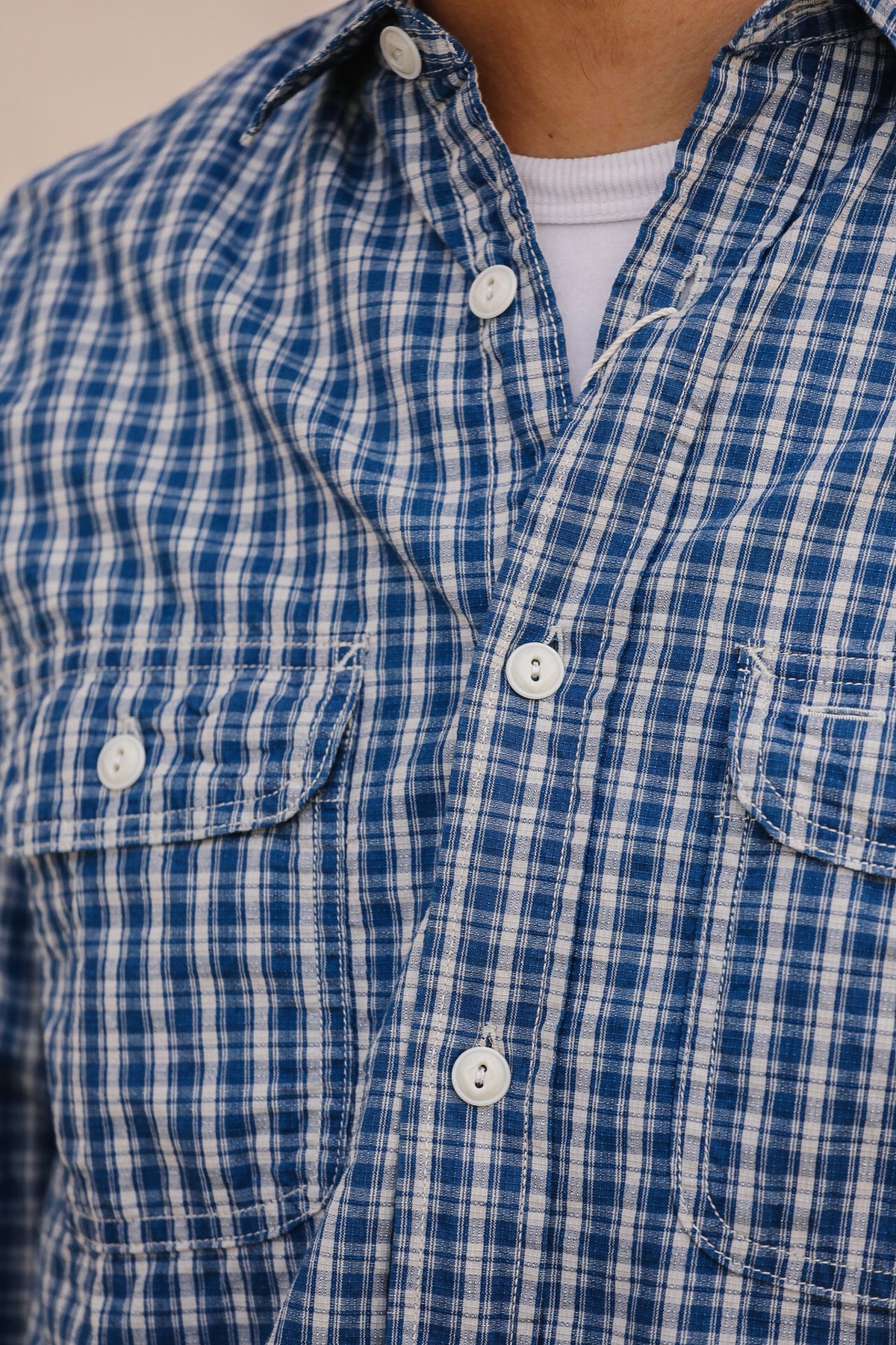 Close-up of a person wearing a blue and white plaid button-down shirt over a white undershirt.