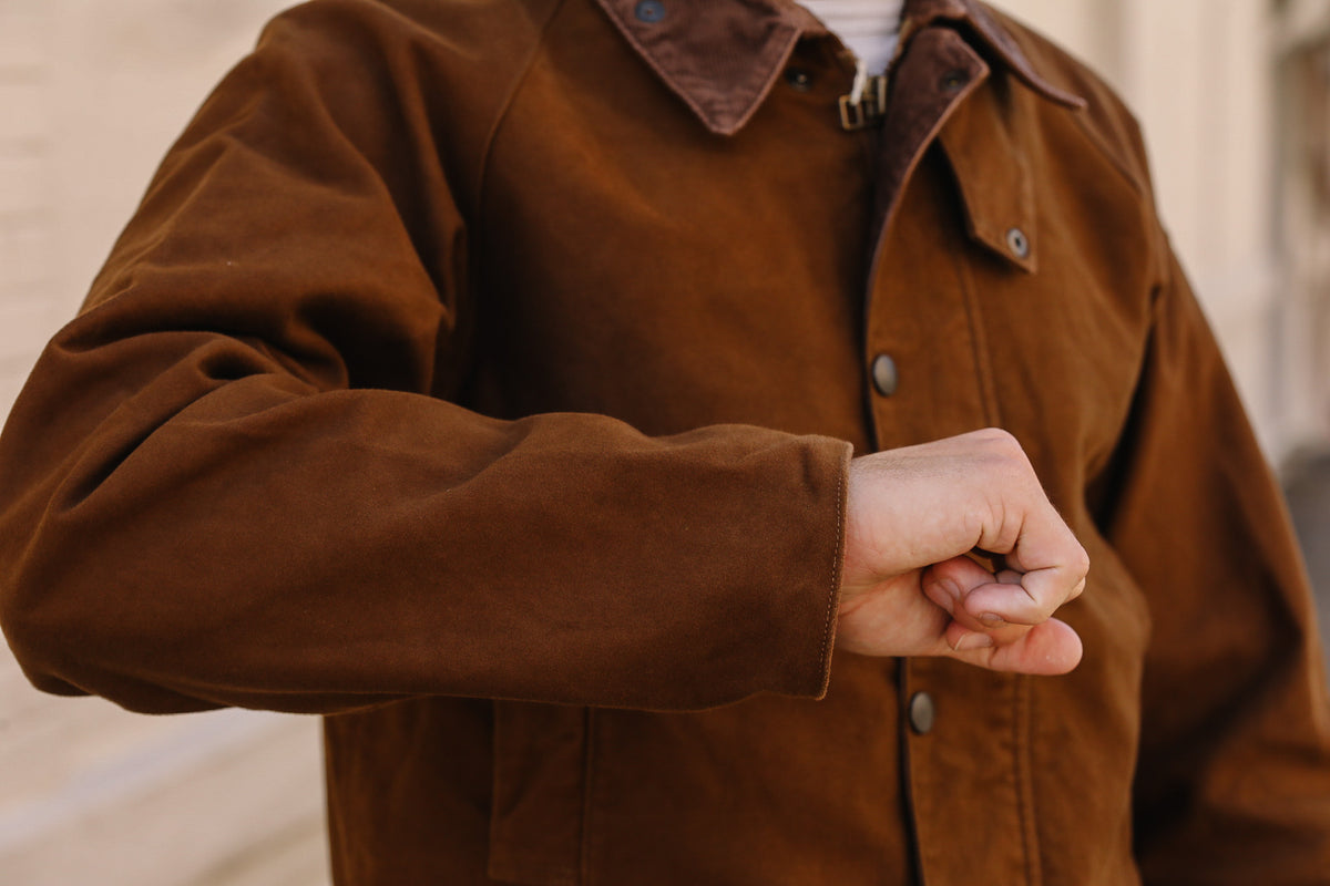 A close-up of a person wearing a brown corduroy jacket, showing the textured fabric and snap-button front, with a blurred outdoor background.