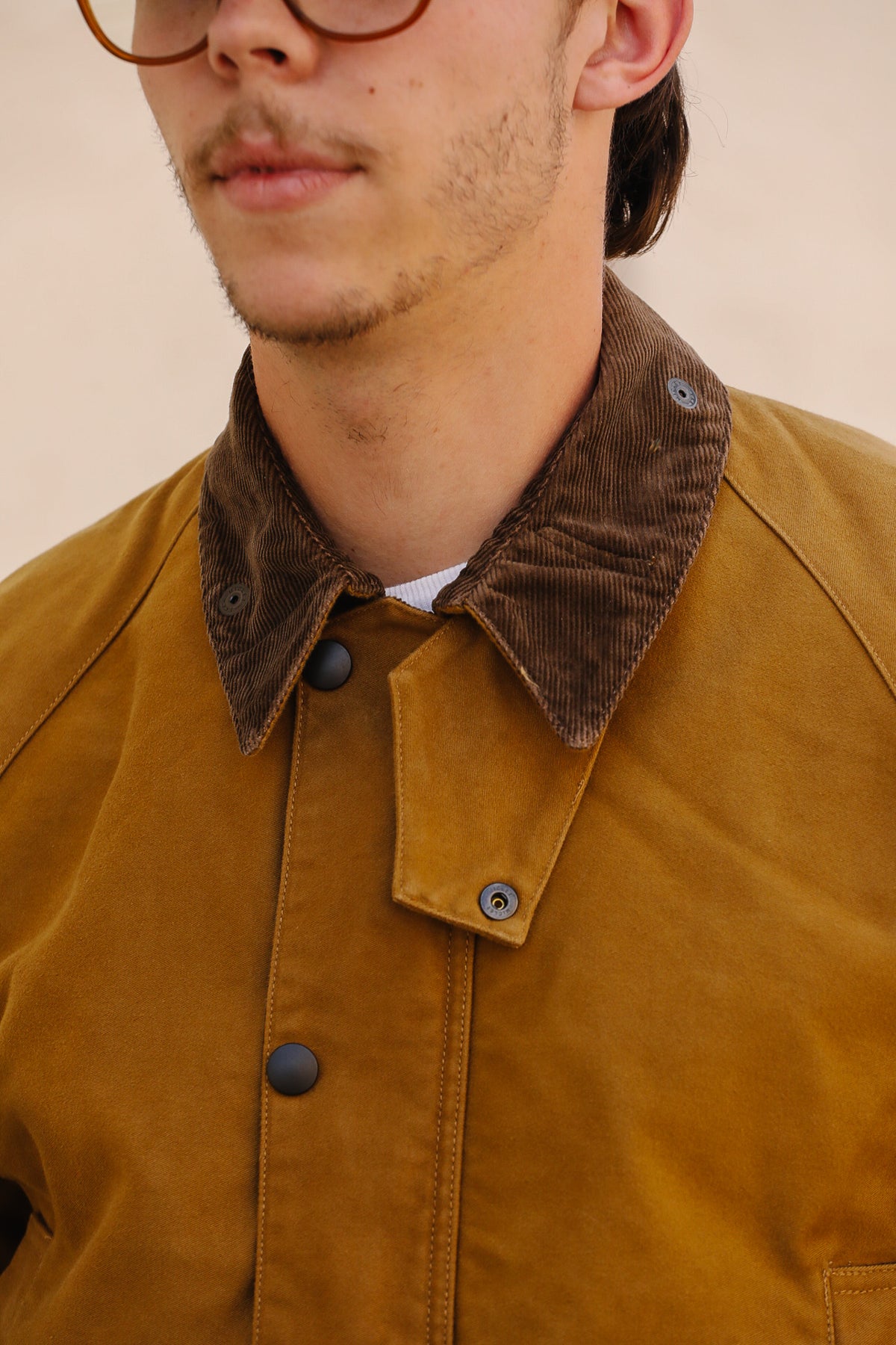 Close-up of a person wearing a mustard yellow corduroy overshirt with a dark brown corduroy collar, featuring dark snap buttons and a white undershirt.