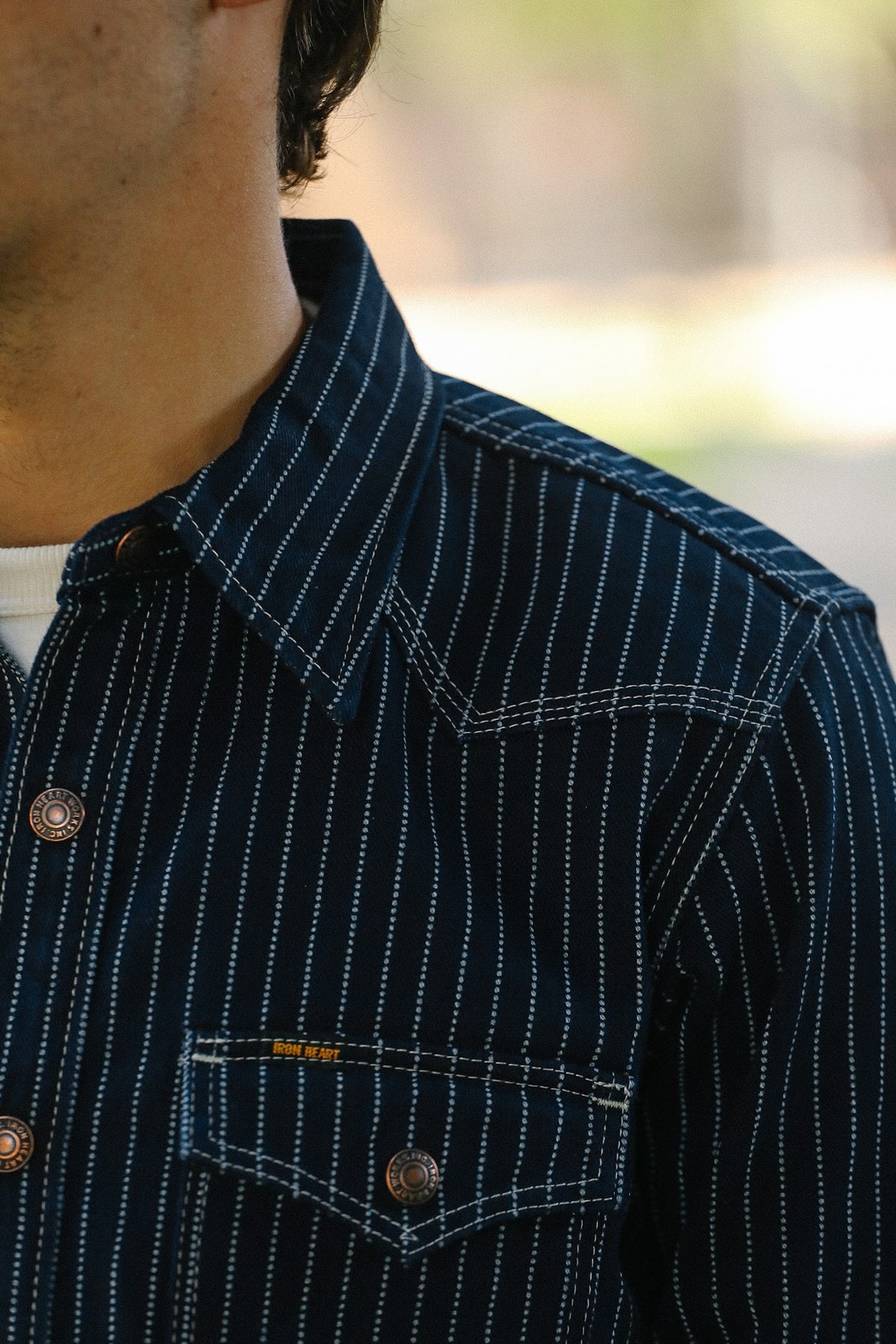 Close-up of a person wearing a dark navy pinstriped denim shirt jacket with white contrast stitching and copper-toned buttons.