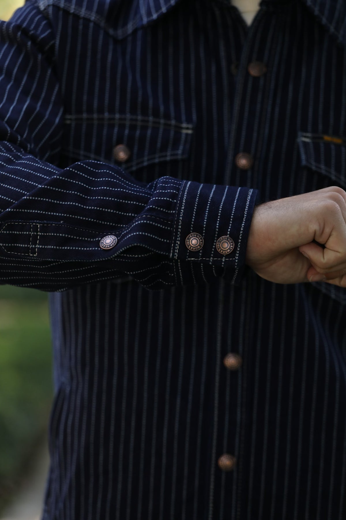 Close-up of a person wearing a dark navy pinstriped button-up shirt with copper-toned buttons and a white undershirt at the collar.