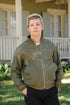 Young man wearing green zip-up jacket with large front pockets standing outdoors near a porch