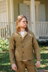 Man wearing brown rugged jacket and matching pants standing outdoors by a house porch