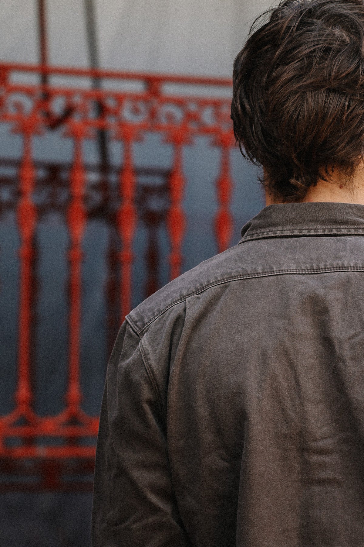 man wearing brown shirt standing in front of metal gate