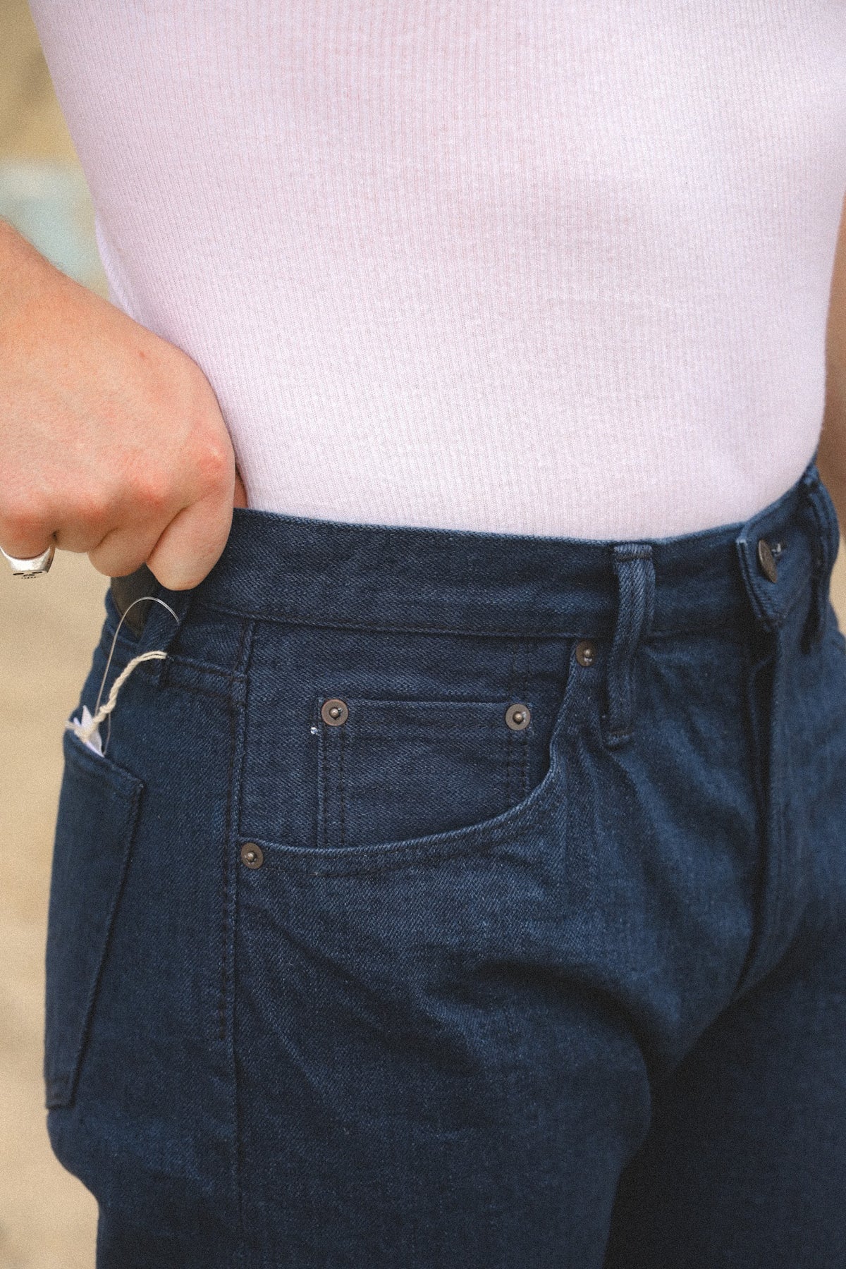 Close-up of a person wearing dark blue denim jeans and a light pink ribbed top, with the hand adjusting the waistband.