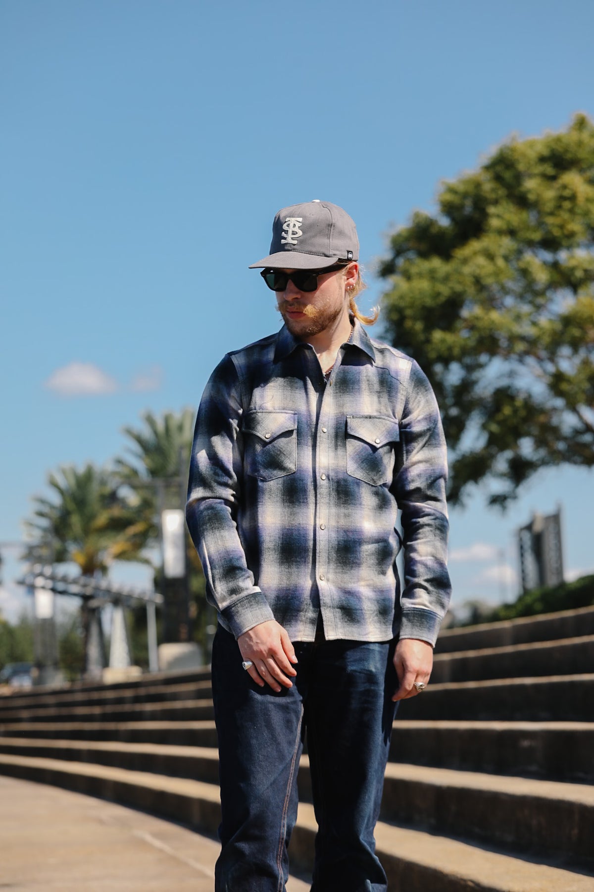 Close-up of a man wearing a blue and gray plaid flannel shirt outdoors, with sunlight casting shadows across the fabric.