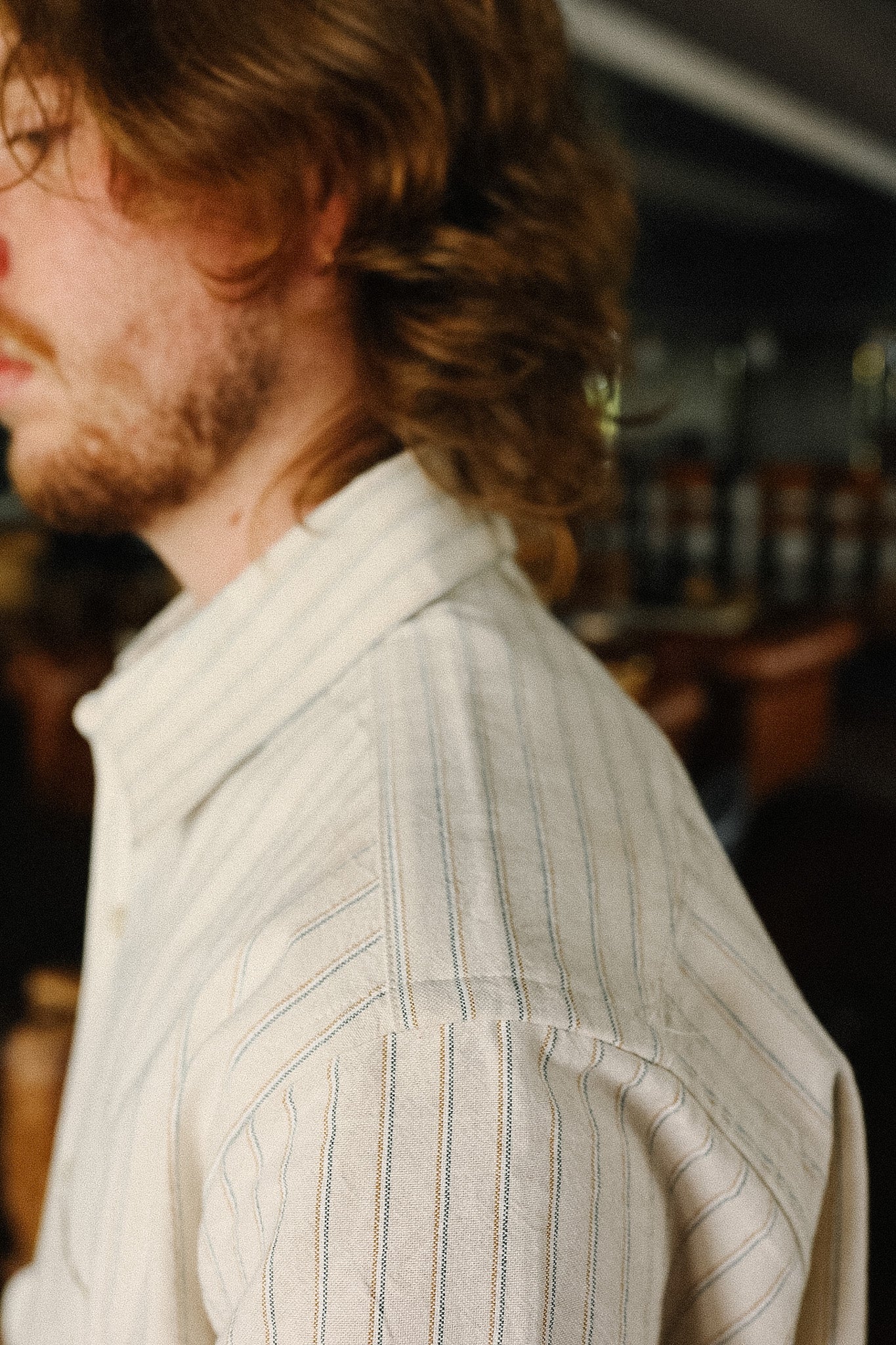 Man with long hair wearing a light-colored striped shirt in an indoor setting.