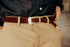 Close-up of brown leather belt with silver buckle worn with beige pants and dark denim shirt
